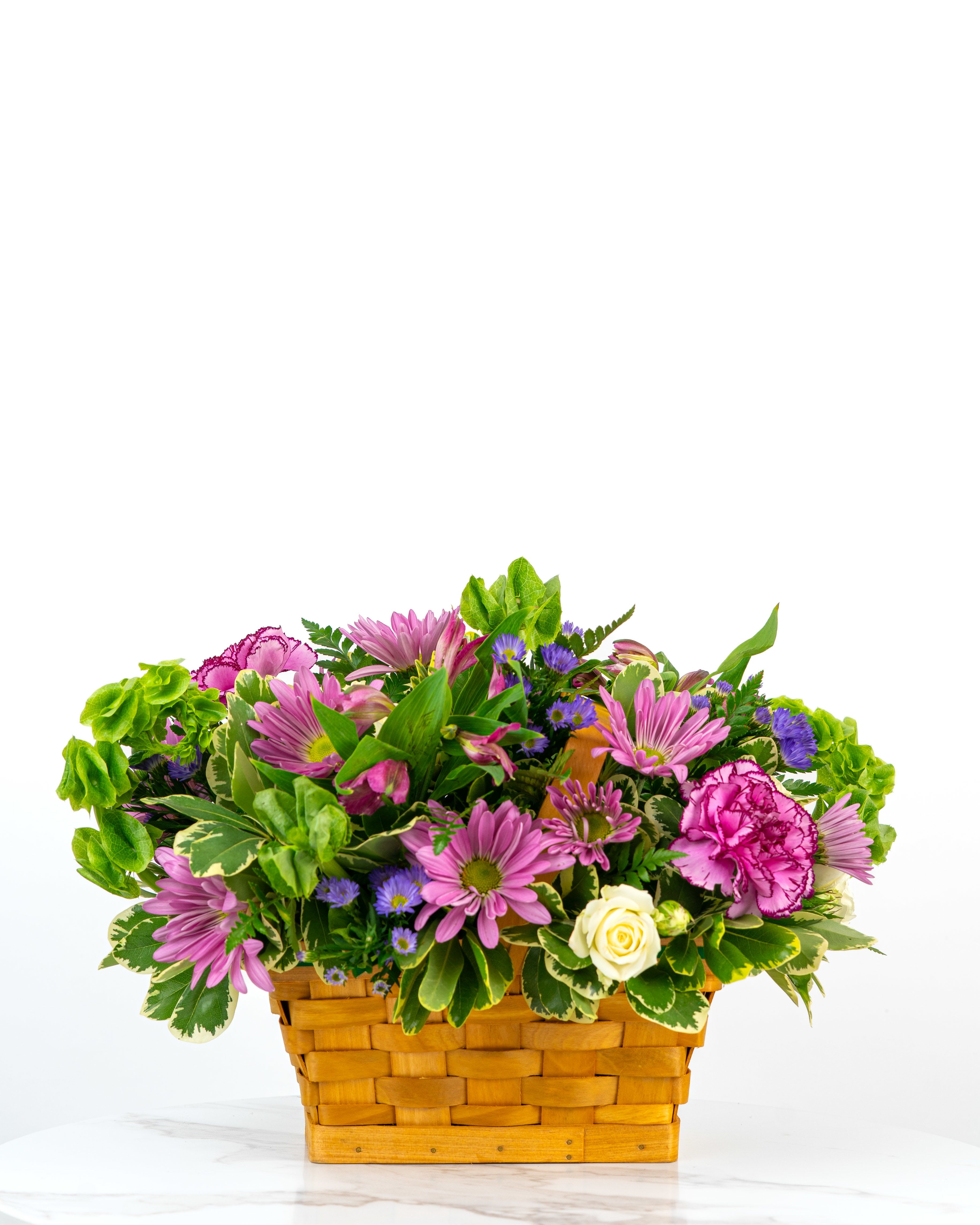 Low basket of pink daisies, purple blooms, green bells of Ireland and a white rose