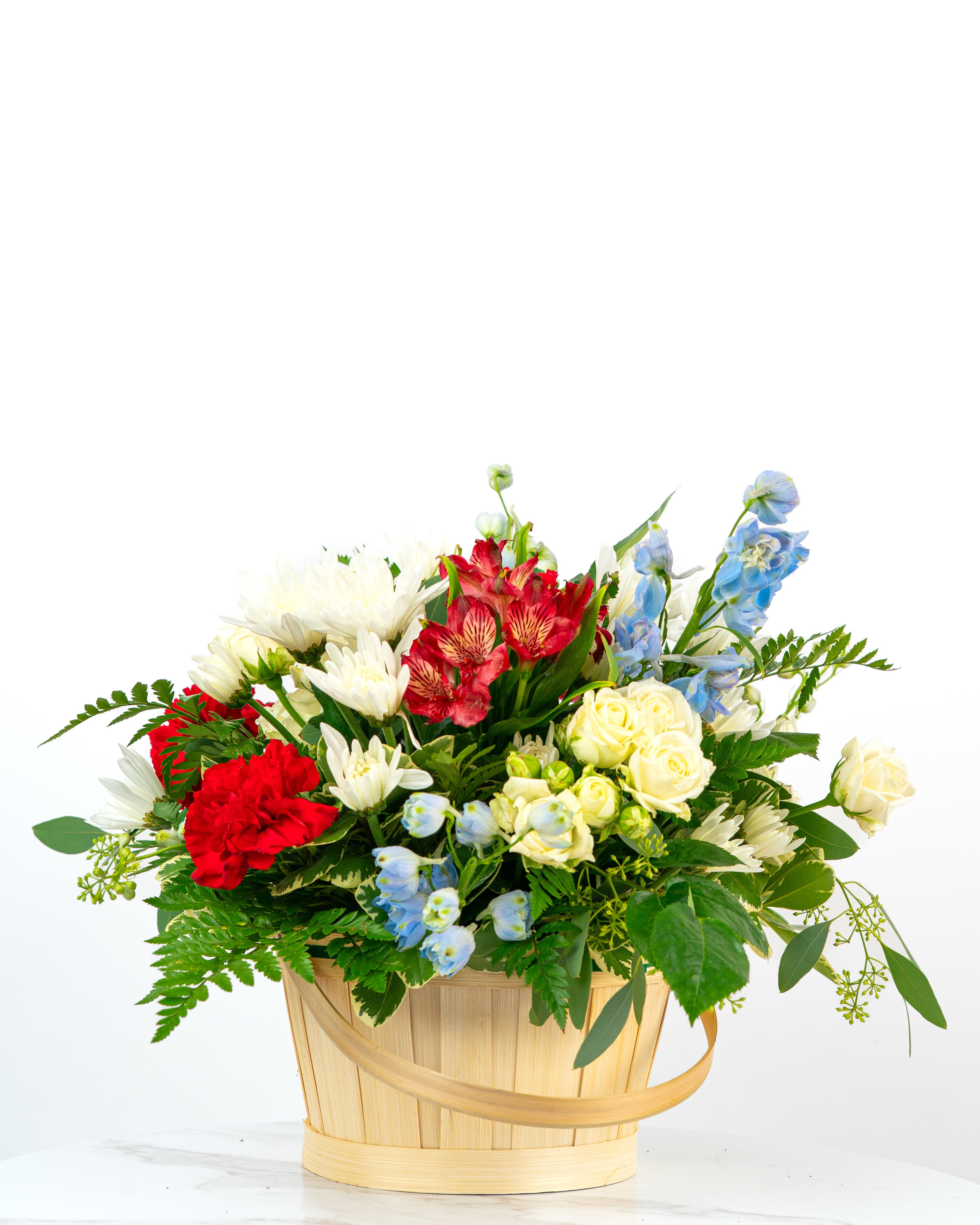 Red, white, yellow, and blue mixed flower basket arrangement in a light wood handled basket