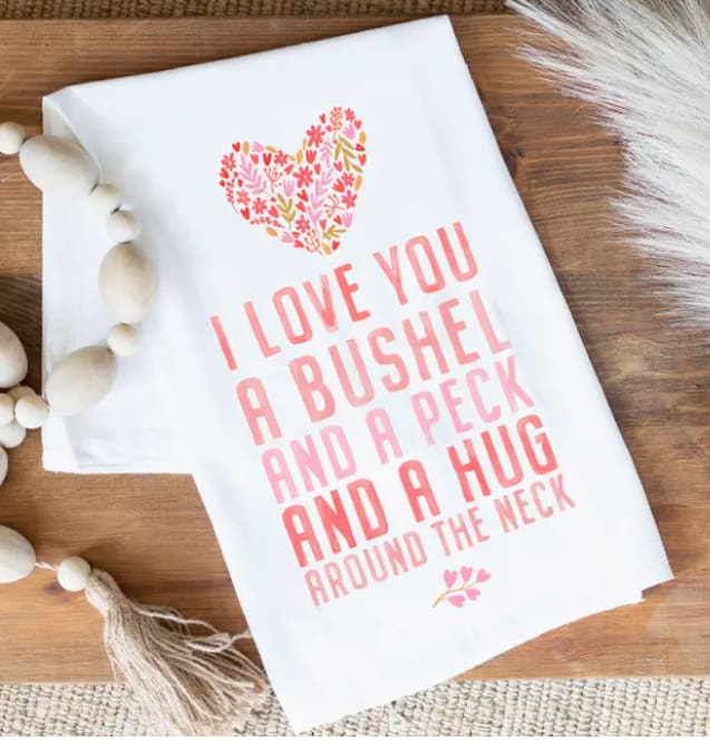 White decorative sign with pink floral heart and text on a wooden surface