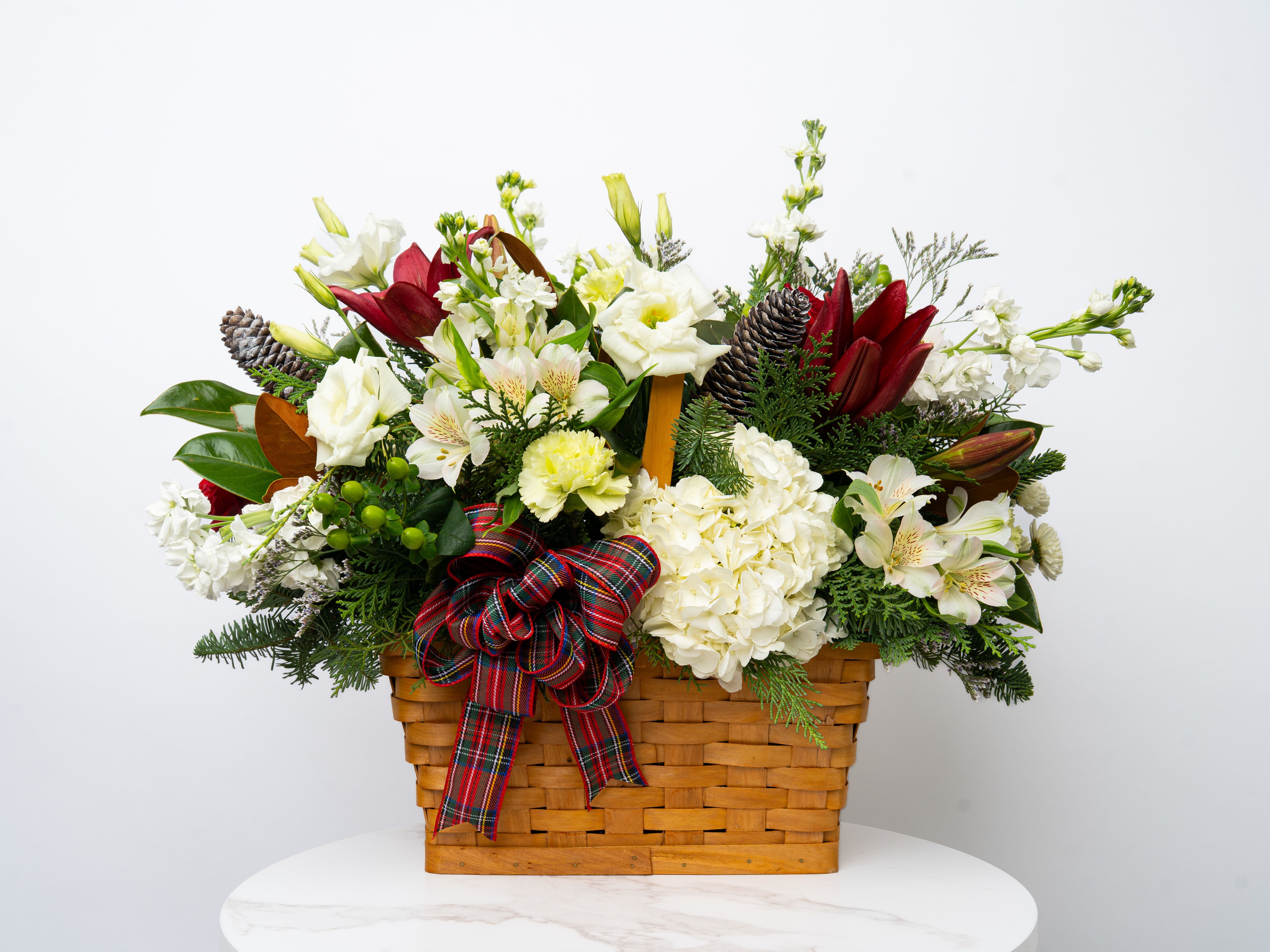 Holiday flower basket with white blooms, red lilies, and a plaid ribbon