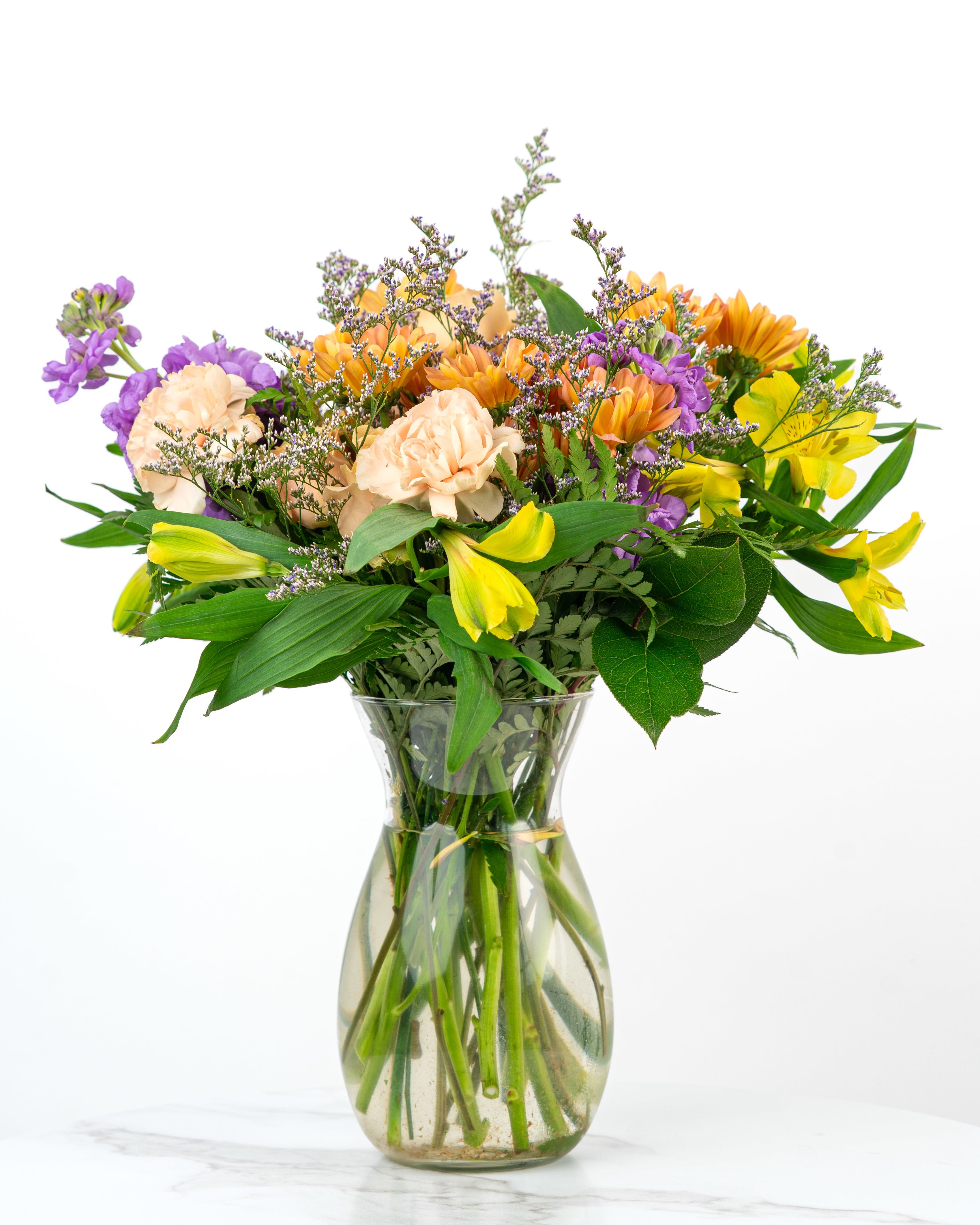 Mixed bouquet of yellow, purple, and peach flowers in a clear glass vase