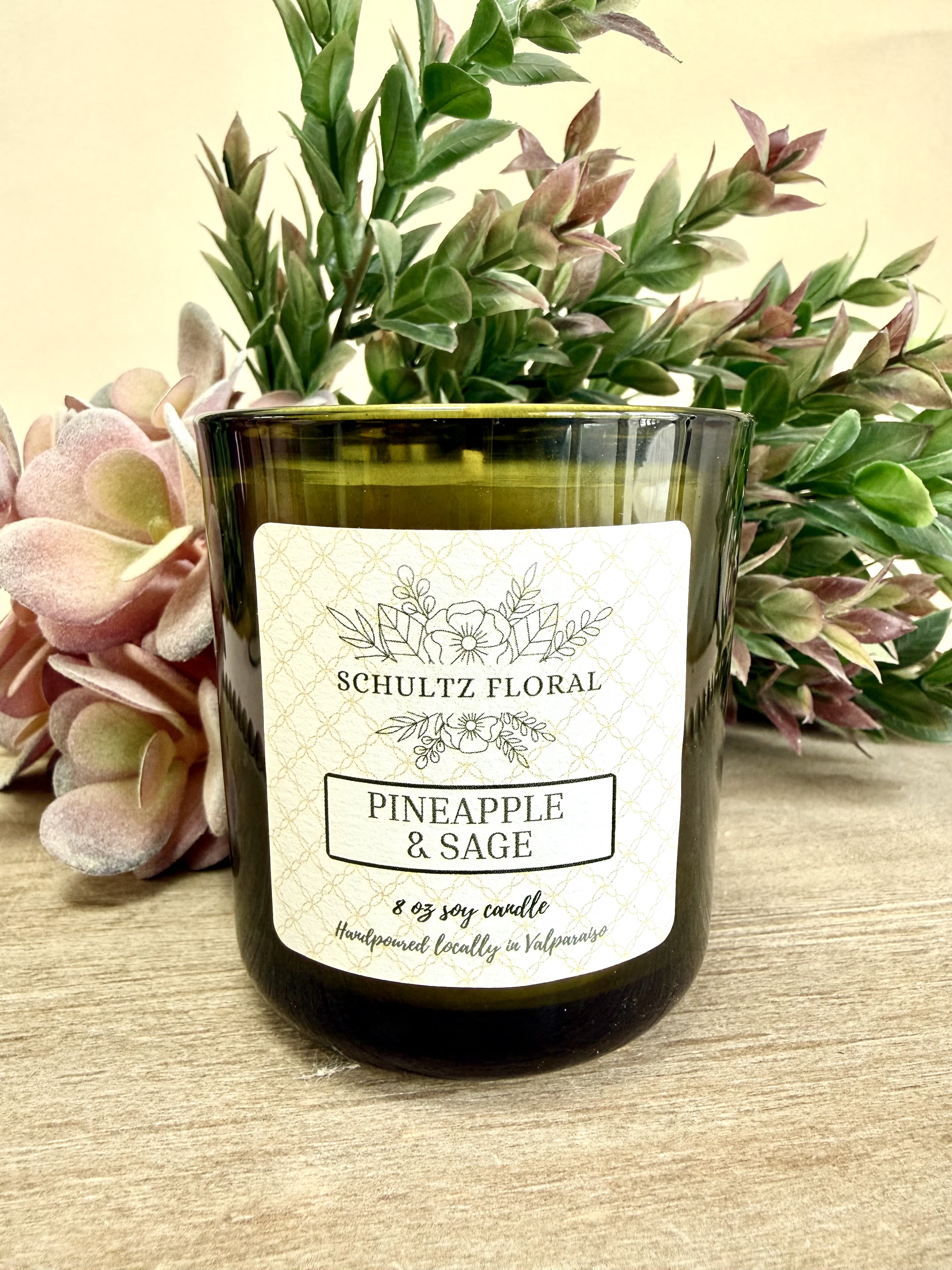 Green glass pineapple and sage candle with decorative foliage behind it