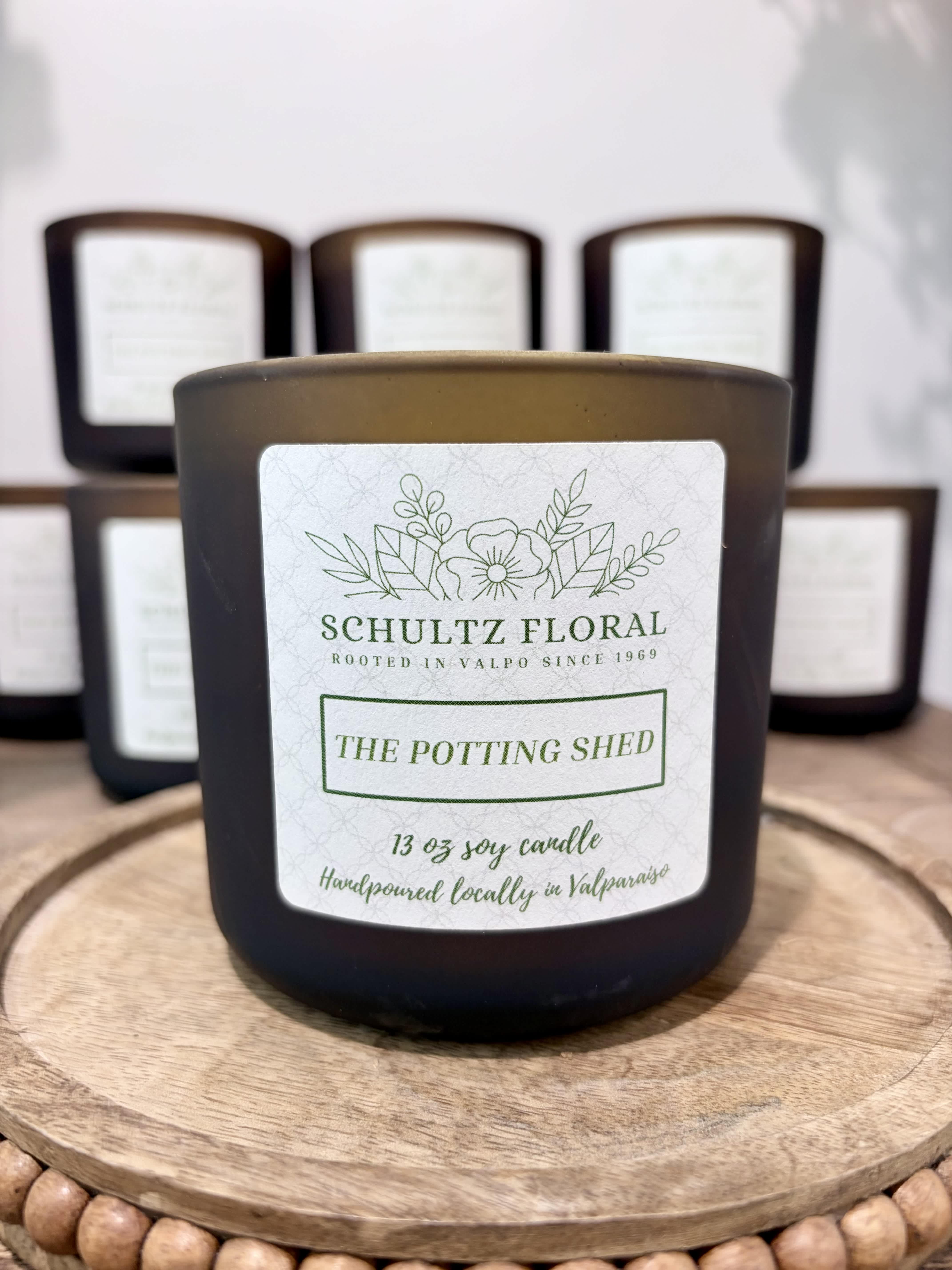 Black jar candle labeled "The Potting Shed" on a wooden tray