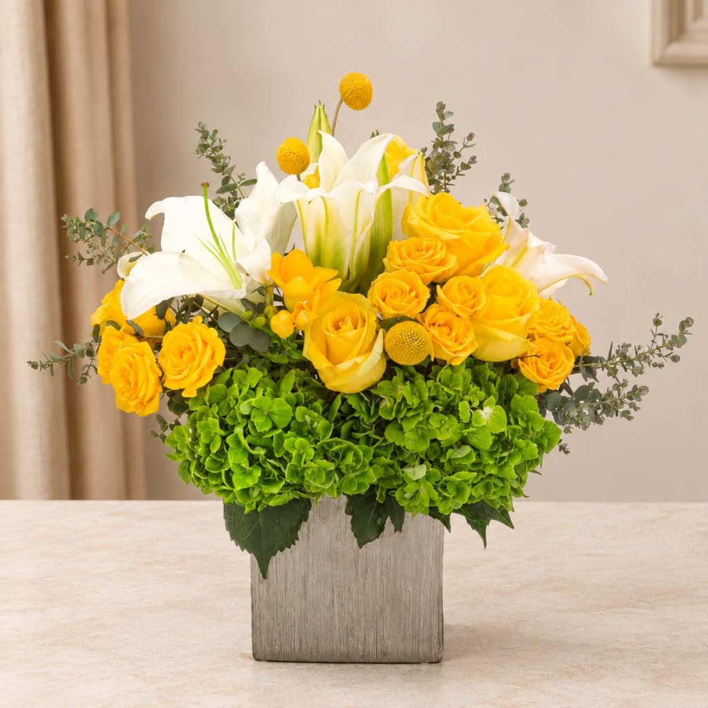 Yellow roses and white lilies in a square vase with green hydrangeas