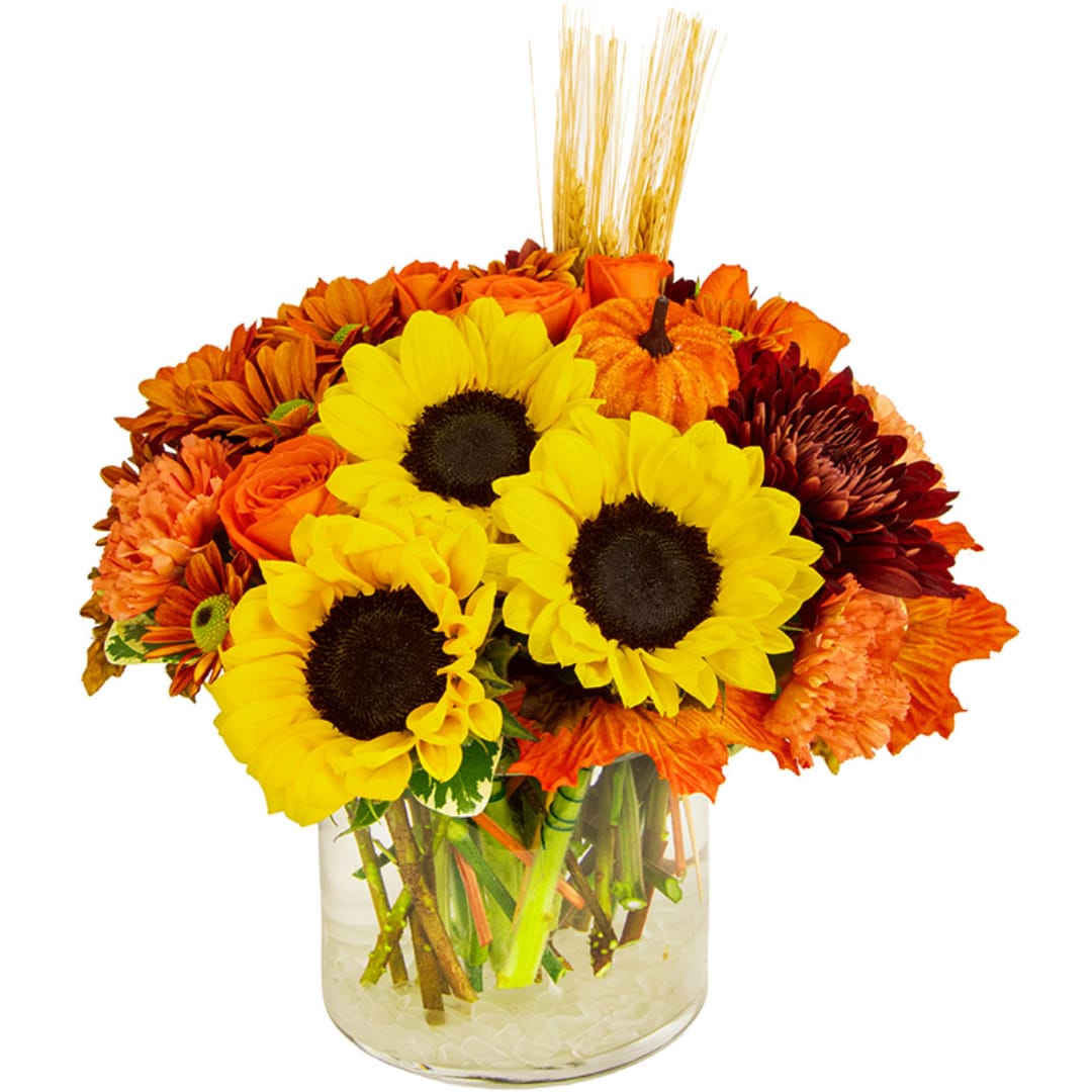 Sunflowers and orange flowers in a clear glass vase with a small pumpkin accent