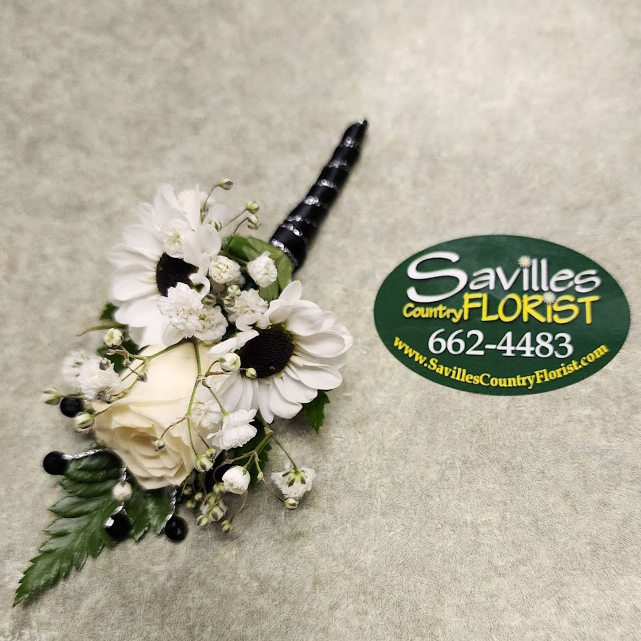 White floral boutonniere with daisies and a rose on a gray surface