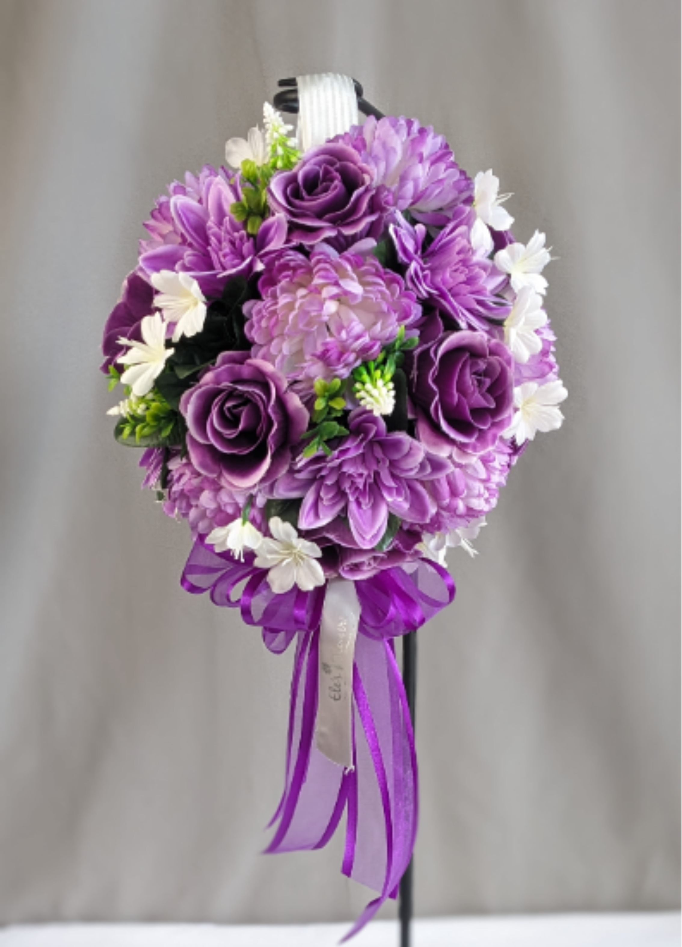 Memorial Topiary - Artificial Arrangement - Honor the memory of a loved one with this beautifully crafted memorial silk floral topiary, thoughtfully designed to bring lasting beauty and remembrance to a graveside, memorial, or special place of reflection. Featuring an elegant blend of soft lavender and rich purple blooms accented with delicate white floral touches and flowing ribbon detail, this arrangement offers a graceful and heartfelt tribute for Memorial Day or year-round remembrance. Crafted with high-end artificial flowers, this weather-resistant design is made to maintain its beauty through the outdoor elements season after season.  The standard option includes the floral topiary arrangement only, while the deluxe option includes the decorative display stand shown, creating an elevated and elegant presentation perfect for cemetery placement or memorial displays.  We would be happy to deliver this to your loved one's gravestone, please provide information on location in the special instructions or give us a call at 715.644.3537  Approximate Dimensions: 31" Diameter (Floral Topiary Size)