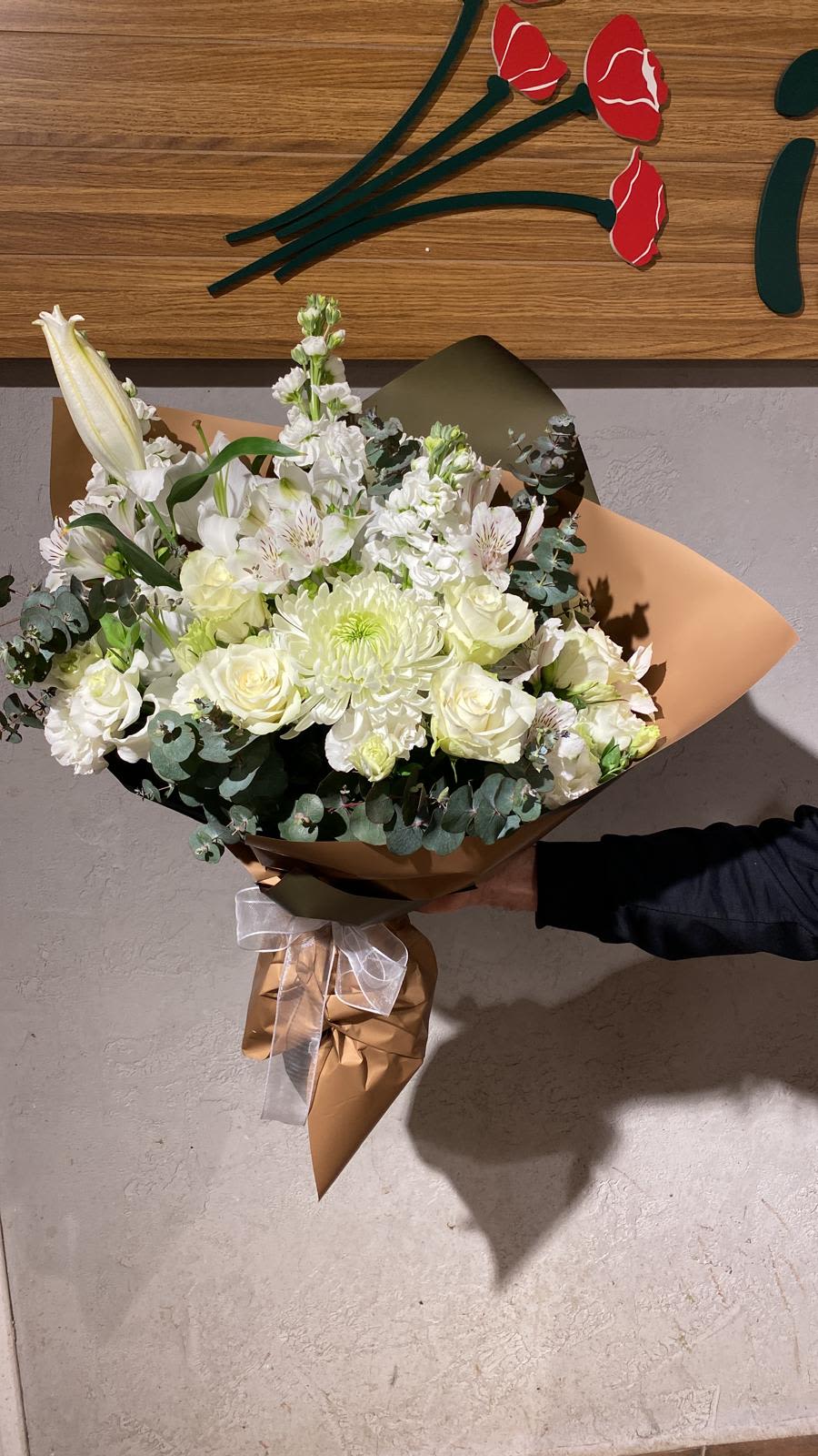 White bouquet with roses, lilies, and chrysanthemums wrapped in brown paper