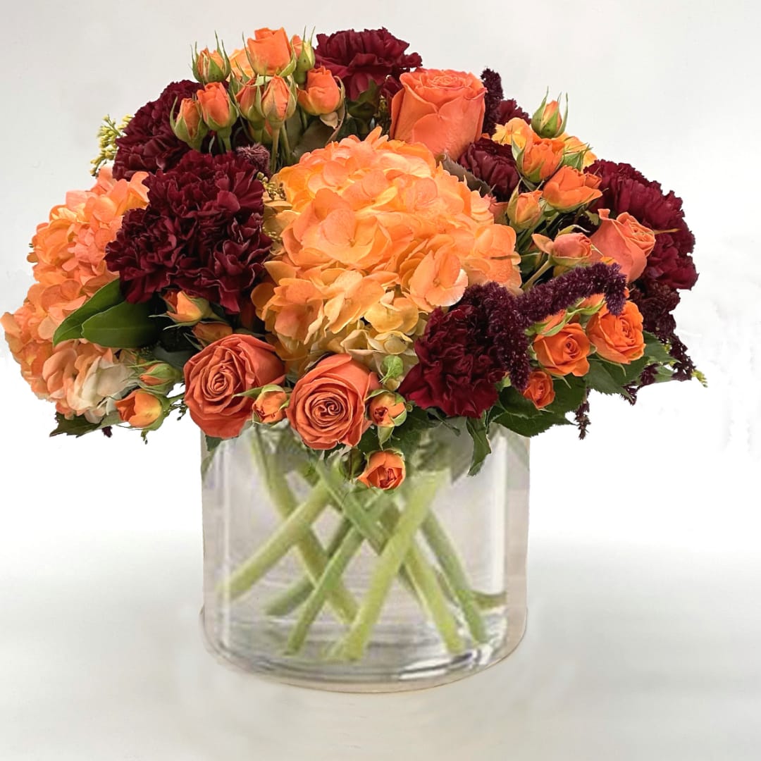 Orange and burgundy flowers arranged in a clear glass vase