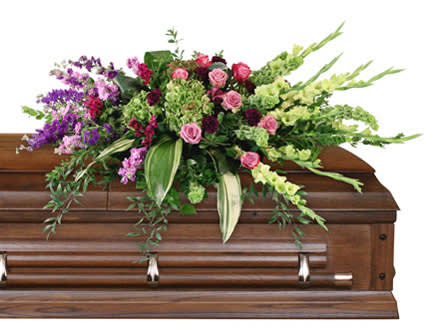 CALMING MEMORIES CASKET SPRAY - Send your loved one off with a radiant spray featuring lush green hues and accents of pink and purple. The Calming Memories casket spray is a tender expression of love ideal for commemorating an elegant woman.