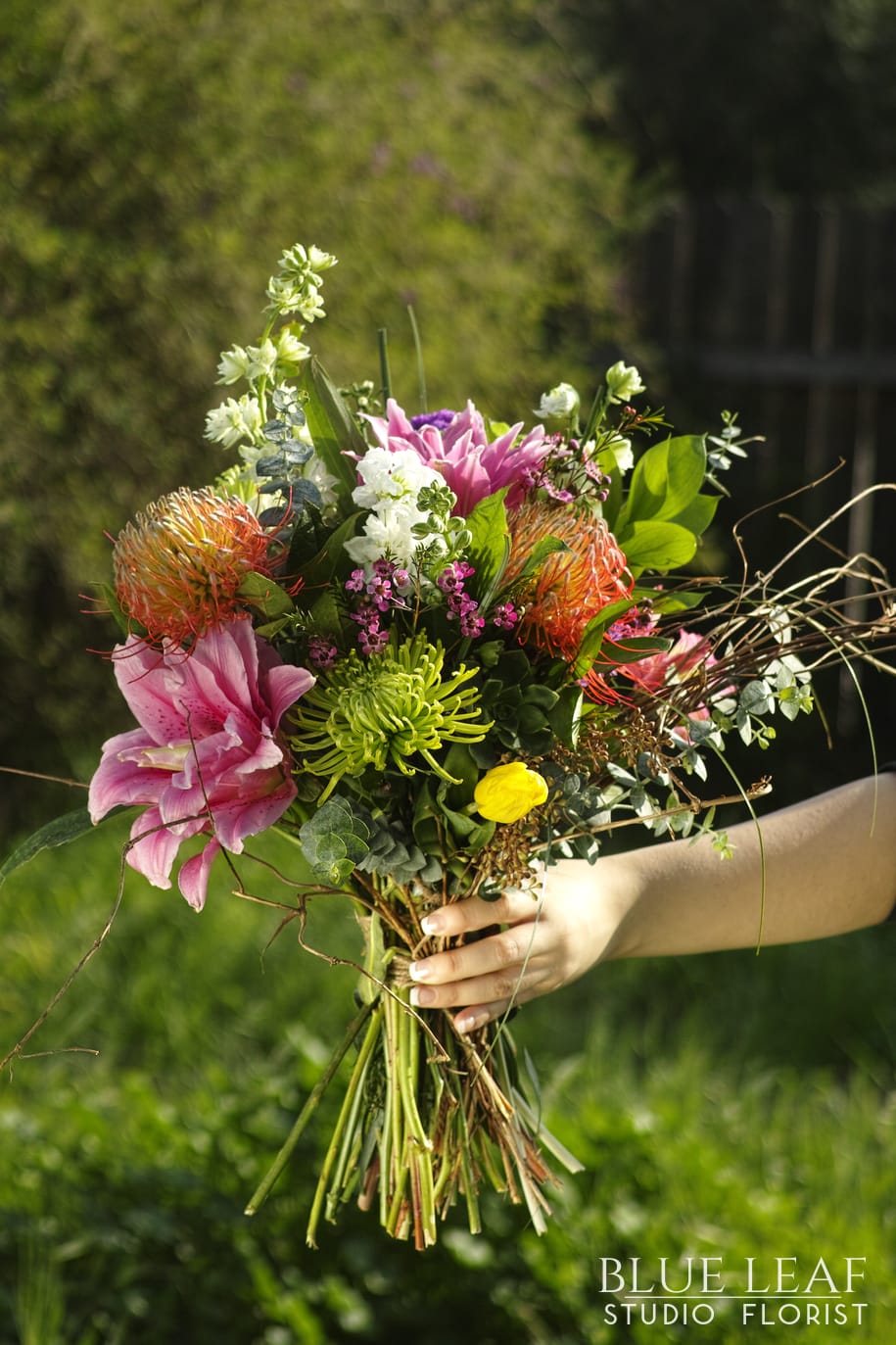 European Garden - Hand-Held Bouquet with a eye-catching mix of flowers such as Protea, Lilies, Larkspur, Spider Mums, Tulips, and Stock. With branches flowing out of it to give it an exotic look (must order 3 days ahead of time to ensure receiving specialty flowers). Hand-wrapped in brown butcher paper.