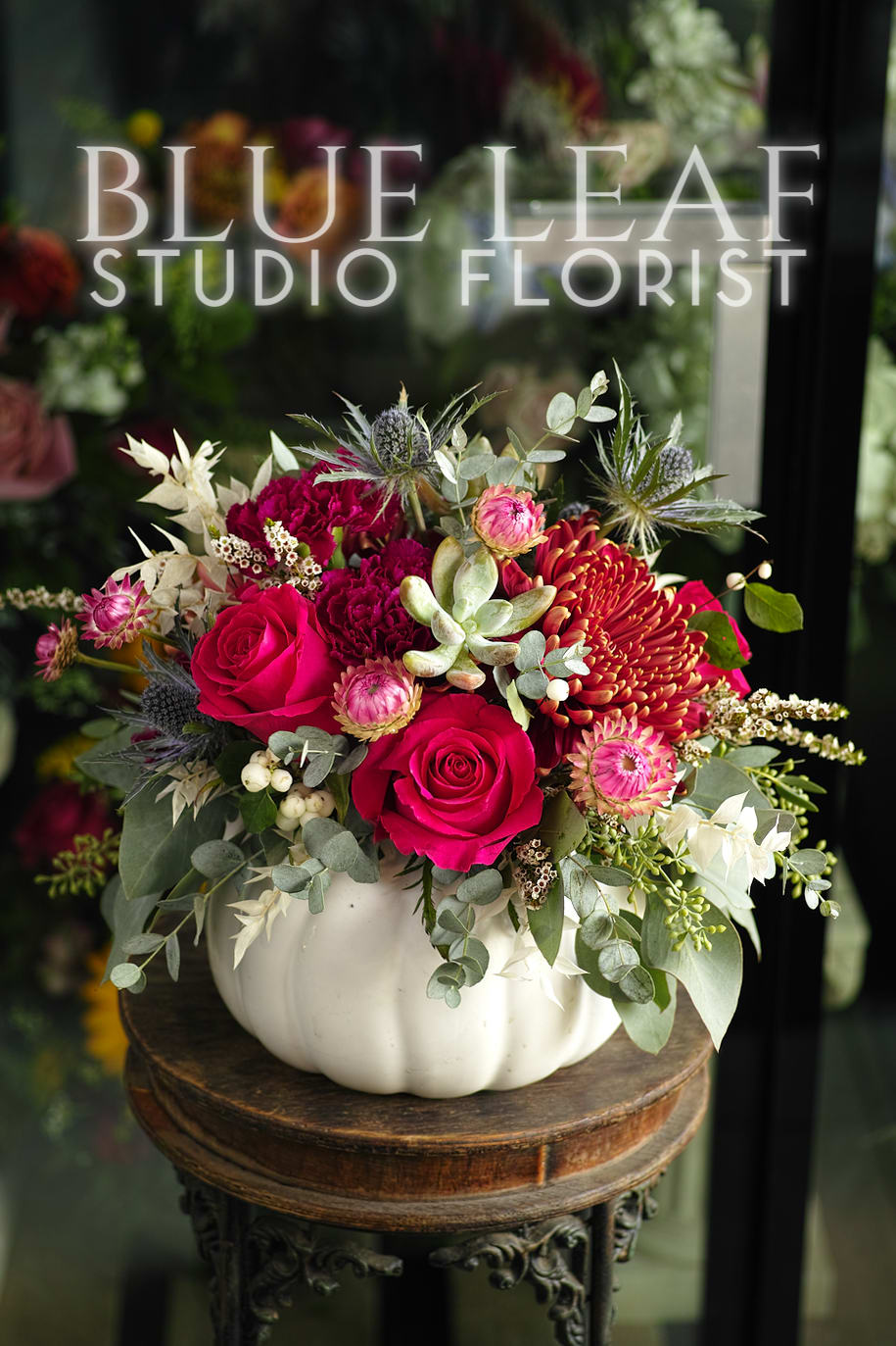 Autumn Berries - A gorgeous, bright arrangement of jewel-toned roses, carnations, succulents, mums, and an assortment of filler flowers. This design comes in a white ceramic pumpkin vase, perfect as a centerpiece for Thanksgiving or Halloween. 