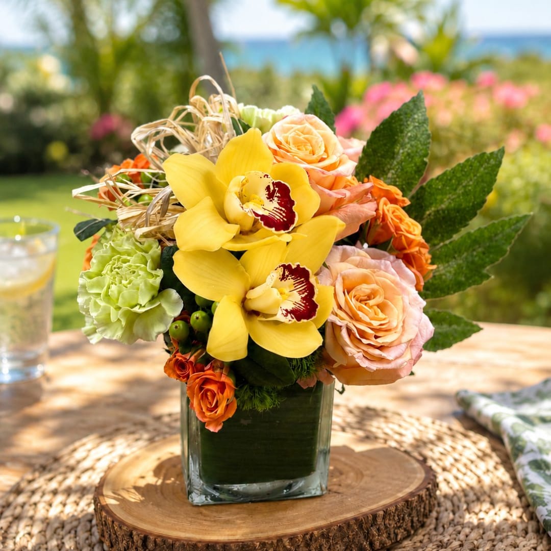 Yellow orchids and peach roses arranged in a square glass vase