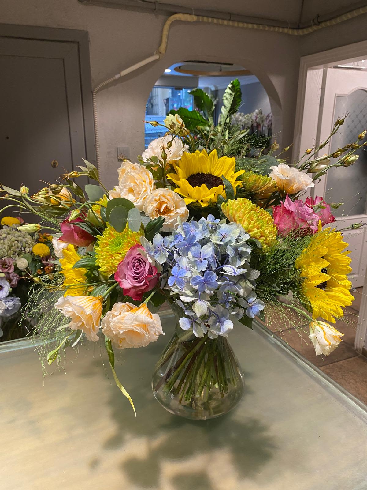 Mixed bouquet with sunflowers, roses, hydrangea, and carnations in a glass vase