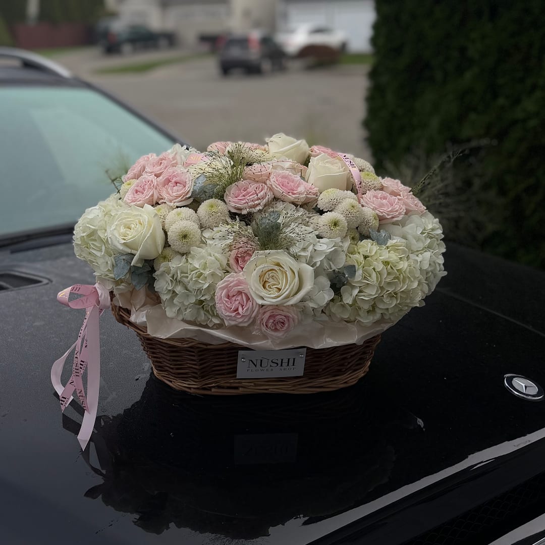 Pink and white roses arranged in a wicker basket on a car hood