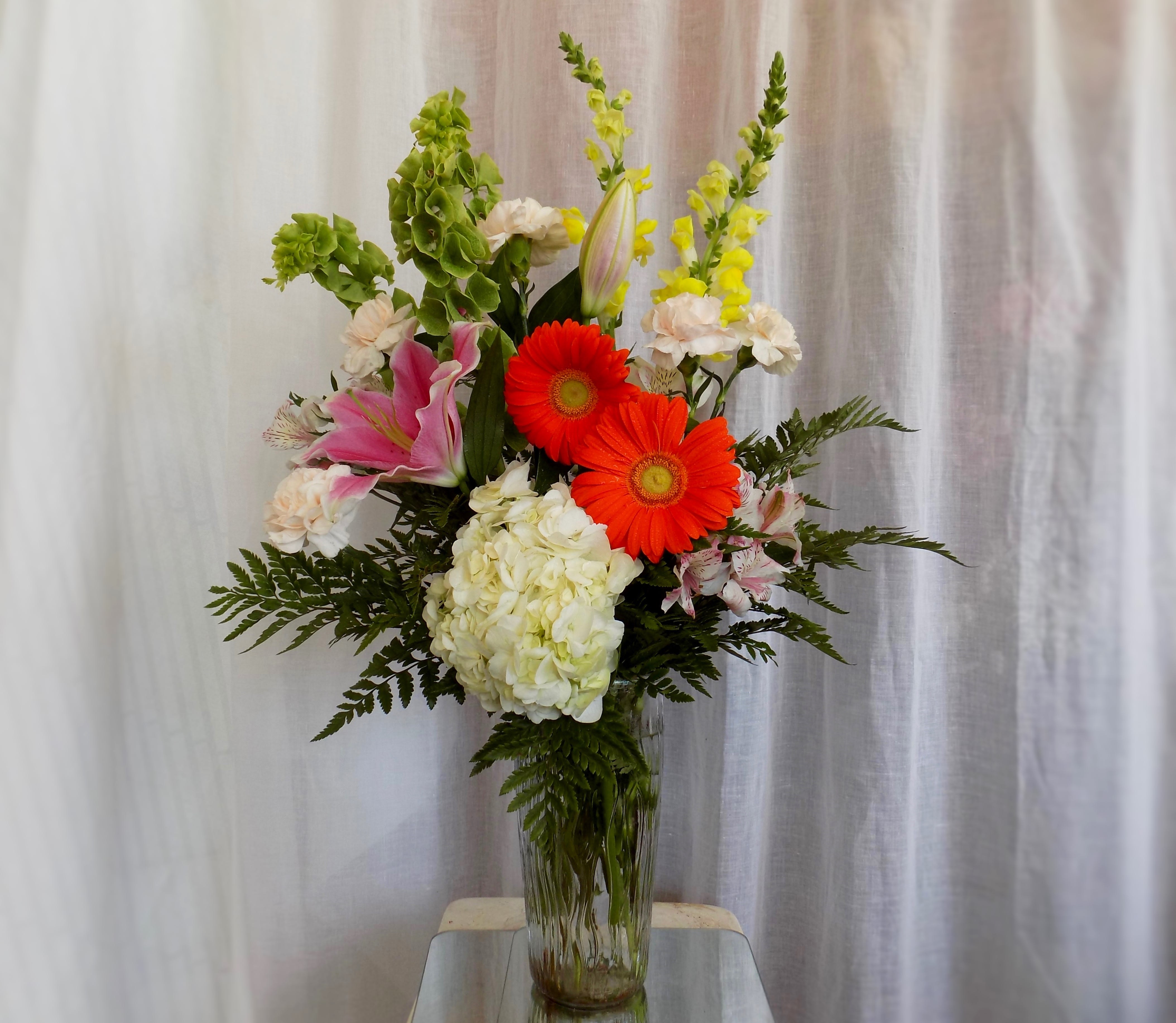 Tall mixed bouquet in a glass vase with pink lilies, orange gerberas, and white hydrangea
