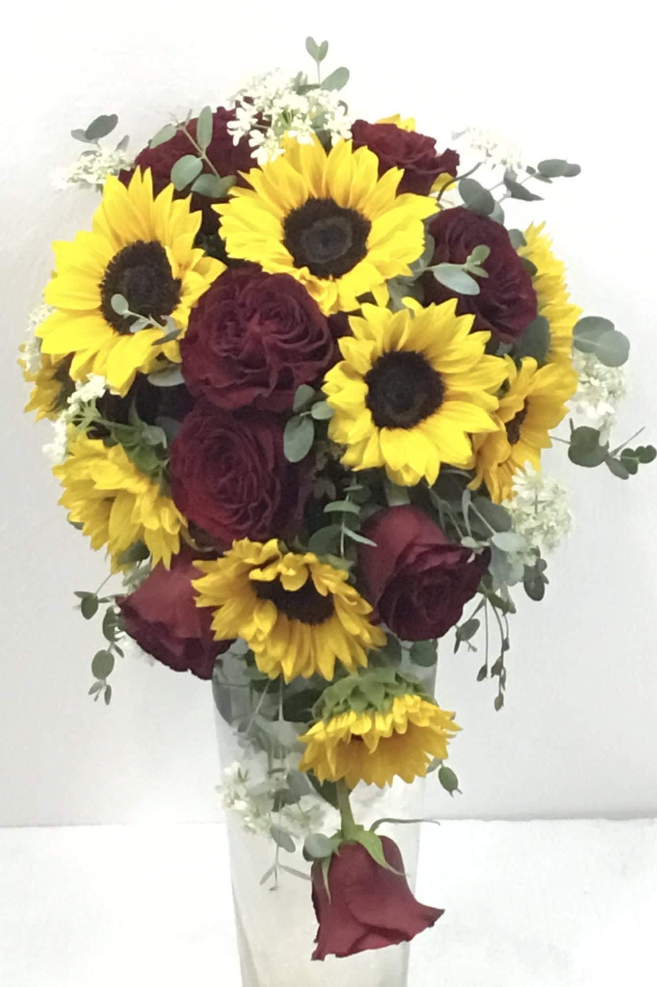 Bouquet of yellow sunflowers and burgundy roses in a clear vase