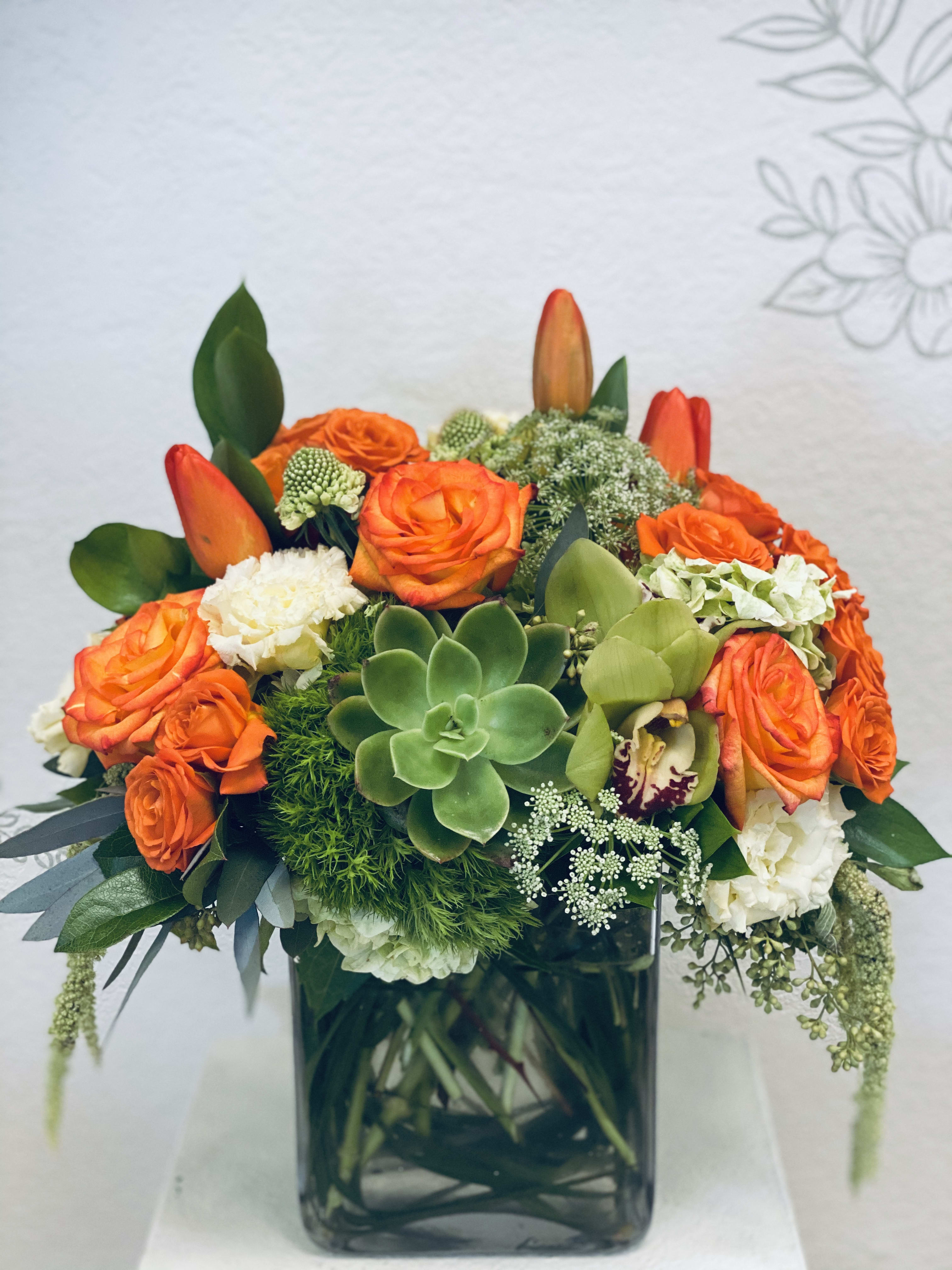 Orange roses and succulents arranged in a square glass vase