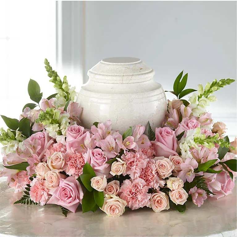 Pink roses and carnations arranged around a white urn.