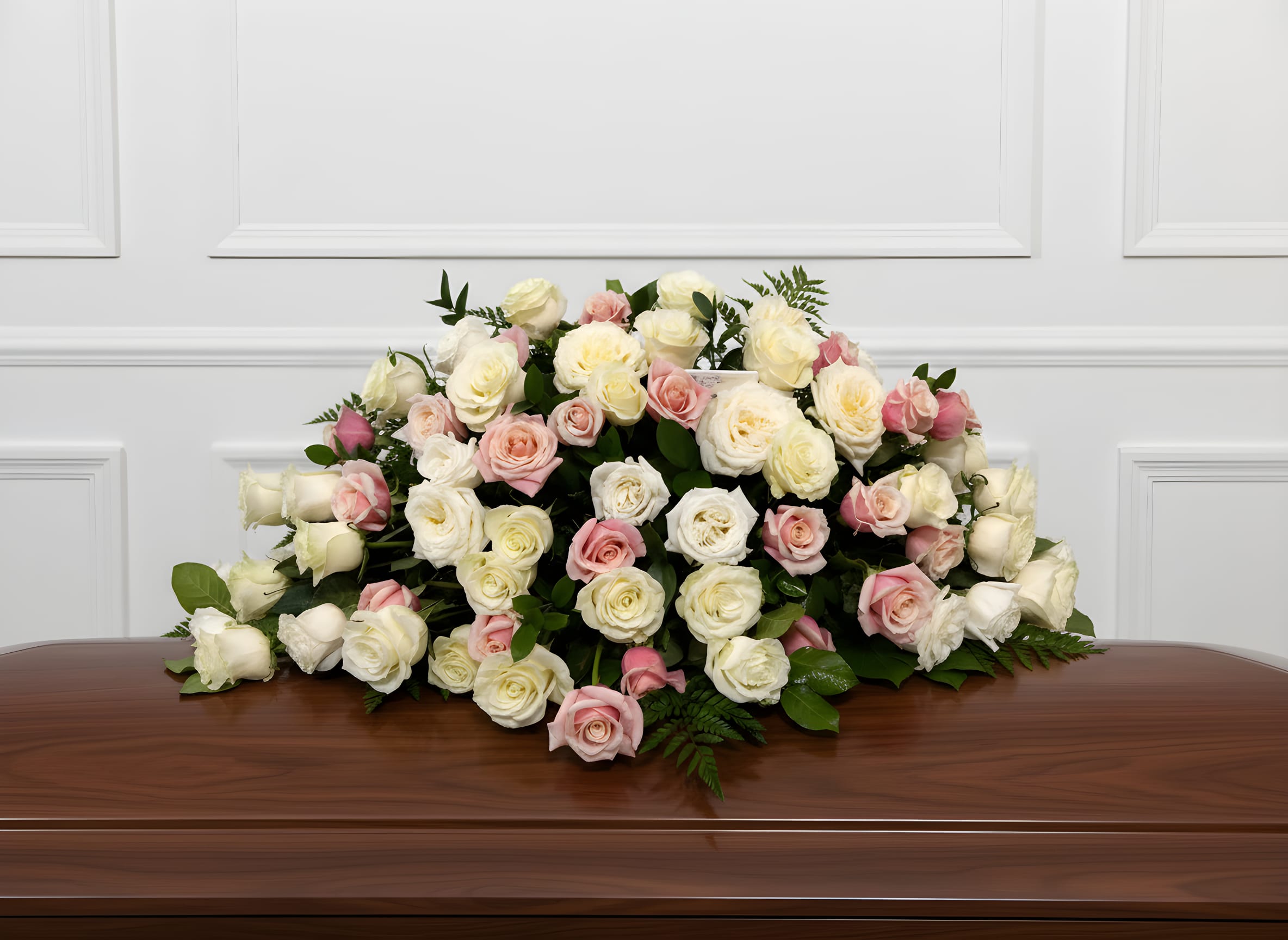 Casket spray of white and blush roses on a wooden casket