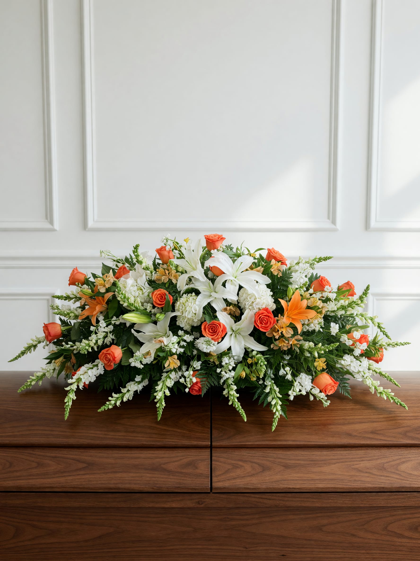 Heaven's Embrace Casket Spray - Celebrate the life of someone deeply loved with our Golden Sunset Casket Spray, a graceful tribute designed to bring warmth, peace, and comfort during a time of remembrance. Casket spray features radiant orange roses, pristine white lilies, white hydrangeas, delicate white snapdragons, and complementary seasonal blooms, beautifully arranged with lush premium greenery.  The vibrant orange roses symbolize admiration, gratitude, and cherished memories, while the white lilies represent peace, innocence, and the soul's return to serenity. Handcrafted by our expert florists, this timeless sympathy arrangement creates a meaningful expression of love and honor, making it a beautiful centerpiece for funeral services, memorial ceremonies, or celebration of life gatherings.