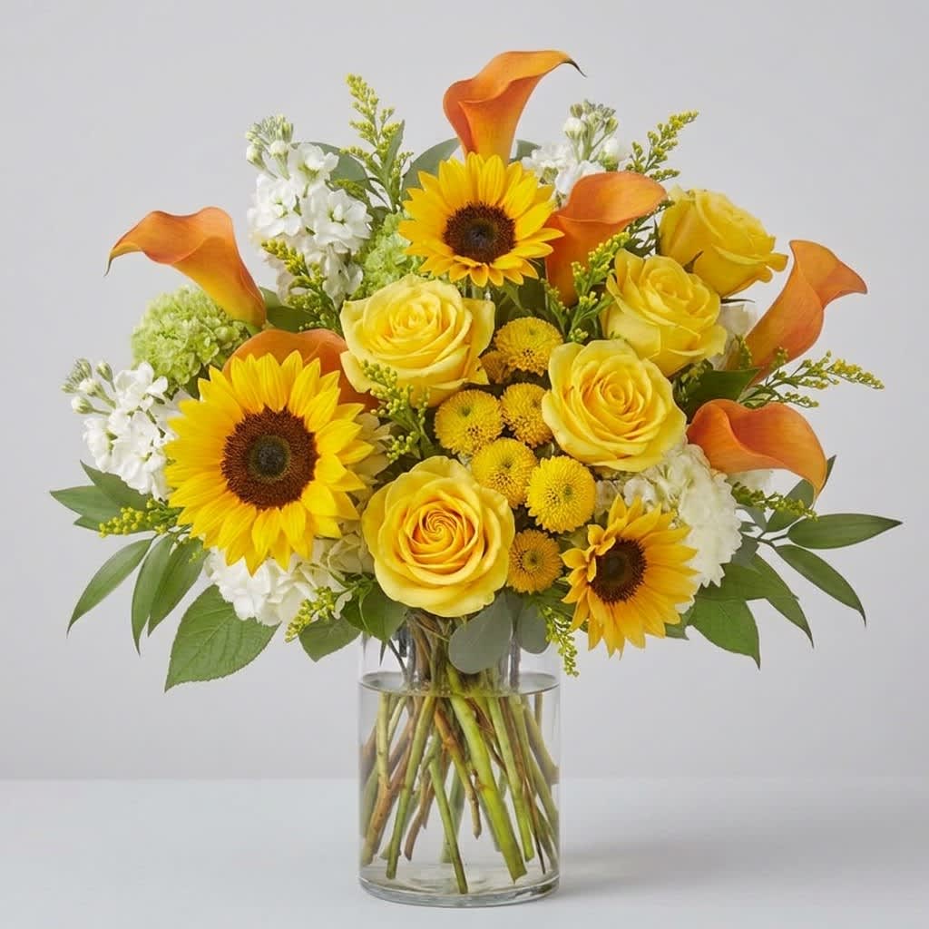 Yellow roses, sunflowers, and orange calla lilies in a glass vase