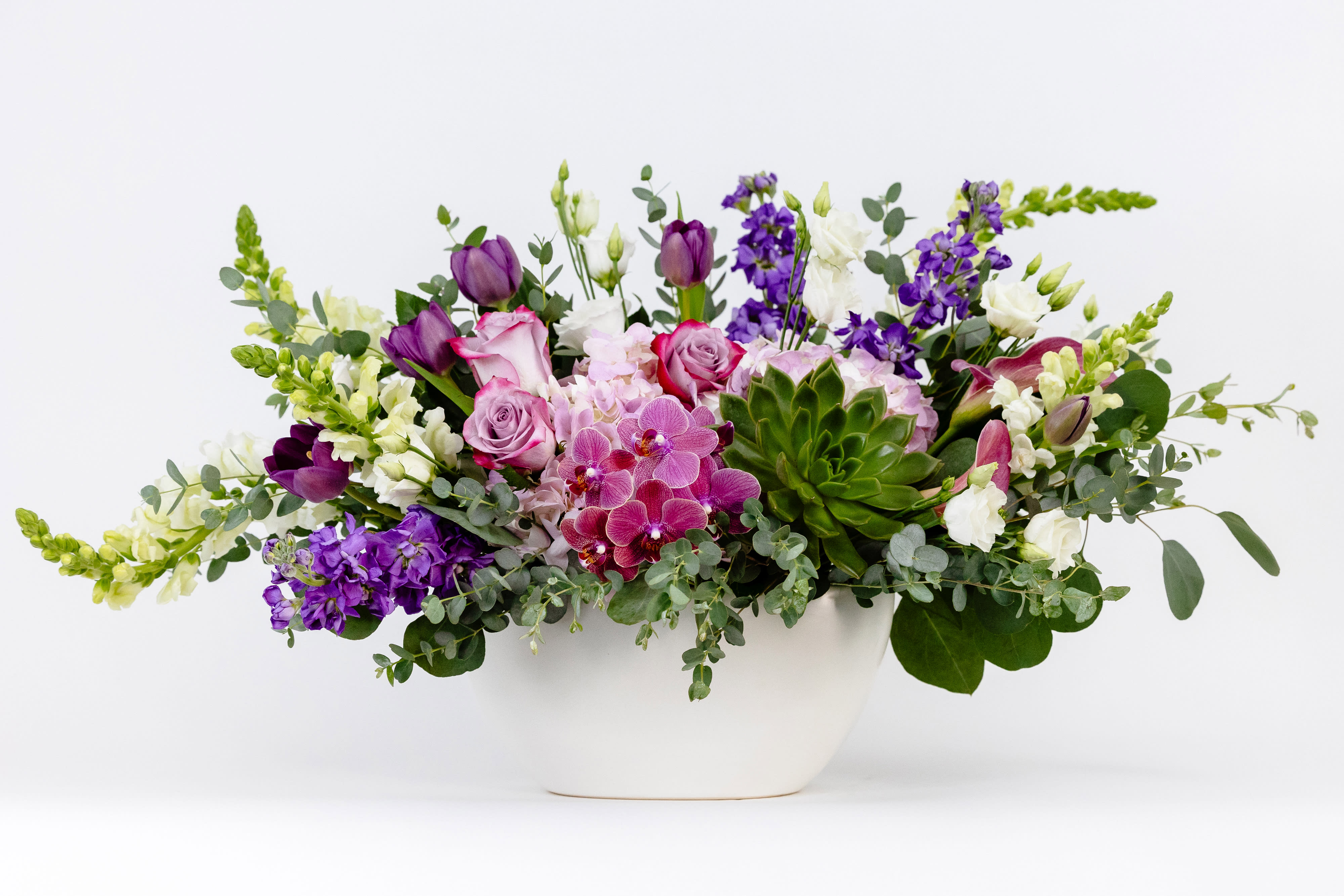 Mixed purple and white floral arrangement in a white bowl vase
