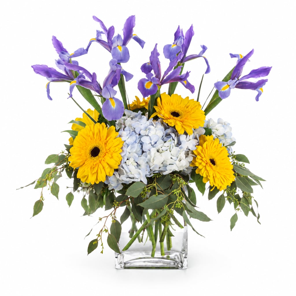 Purple irises and yellow gerbera daisies in a clear square vase