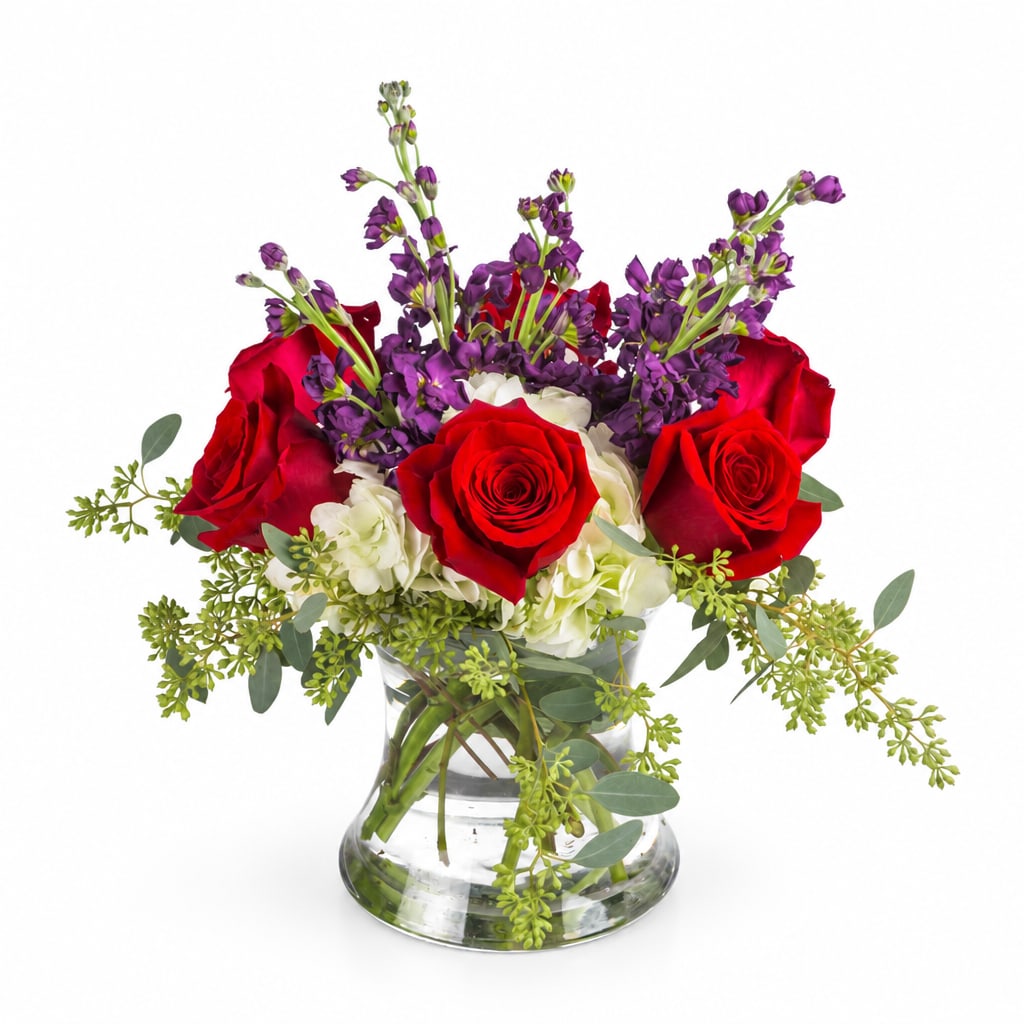 Red roses and purple flowers arranged in a clear glass vase