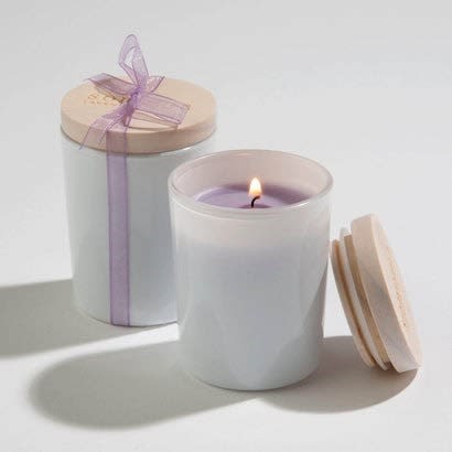Pair of white glass jar candles with wooden lids, one lit and one tied with a lavender ribbon