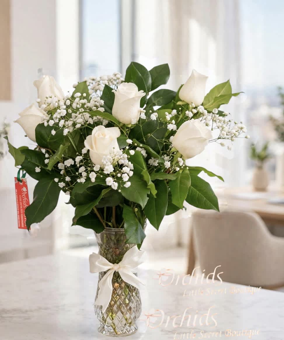 White roses and baby's breath in a clear glass vase with a ribbon