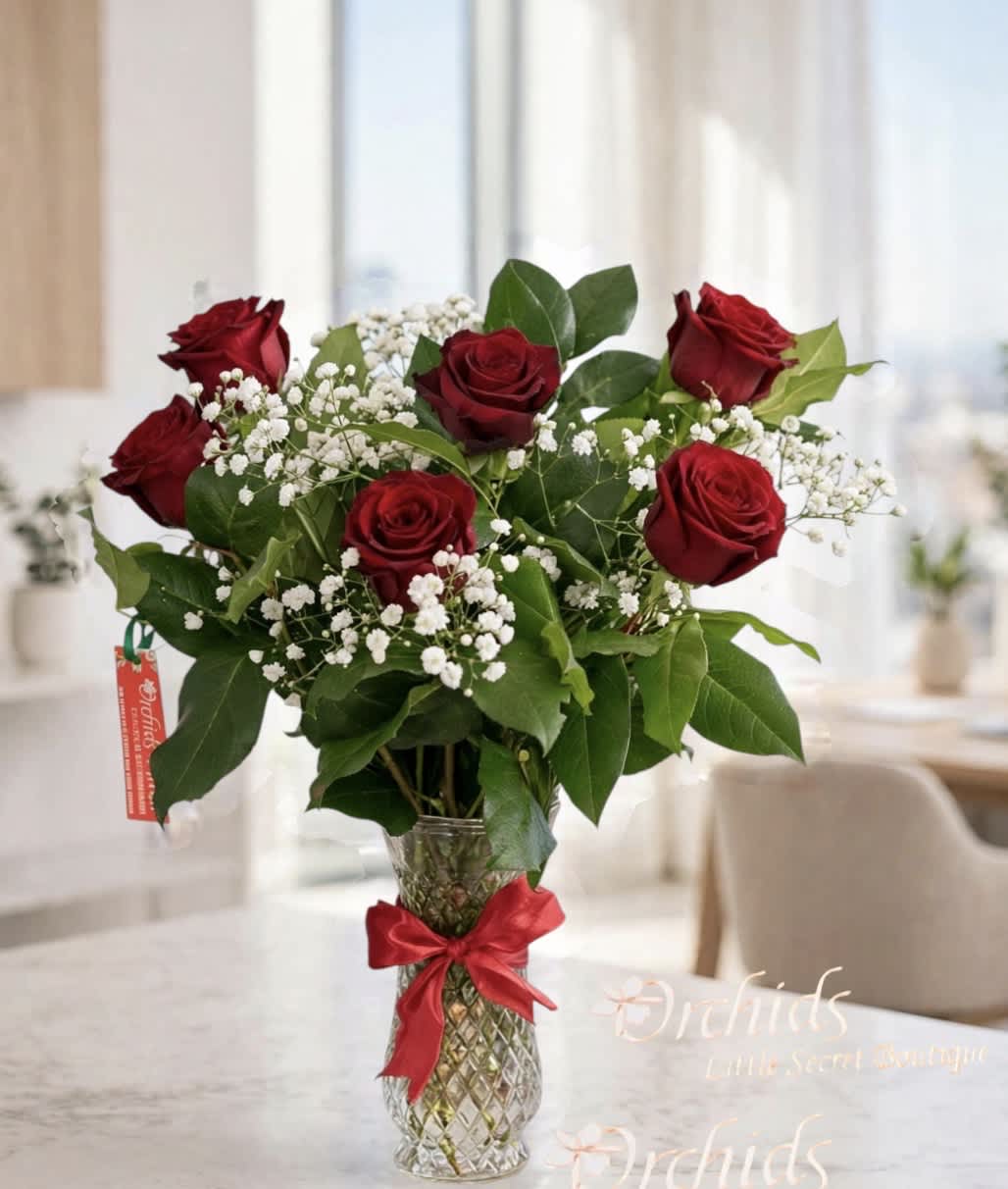 Red roses with white baby's breath in a clear glass vase tied with a red ribbon