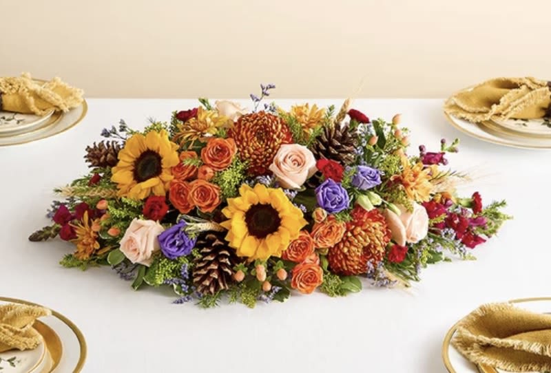 Crisp fall centerpiece - This vibrant centerpiece transforms any table into the setting for a harvest celebration. Sunflowers, roses, lisianthuses, and more blooms in a dazzling array of autumnal colors make this a memorable addition to any gathering.