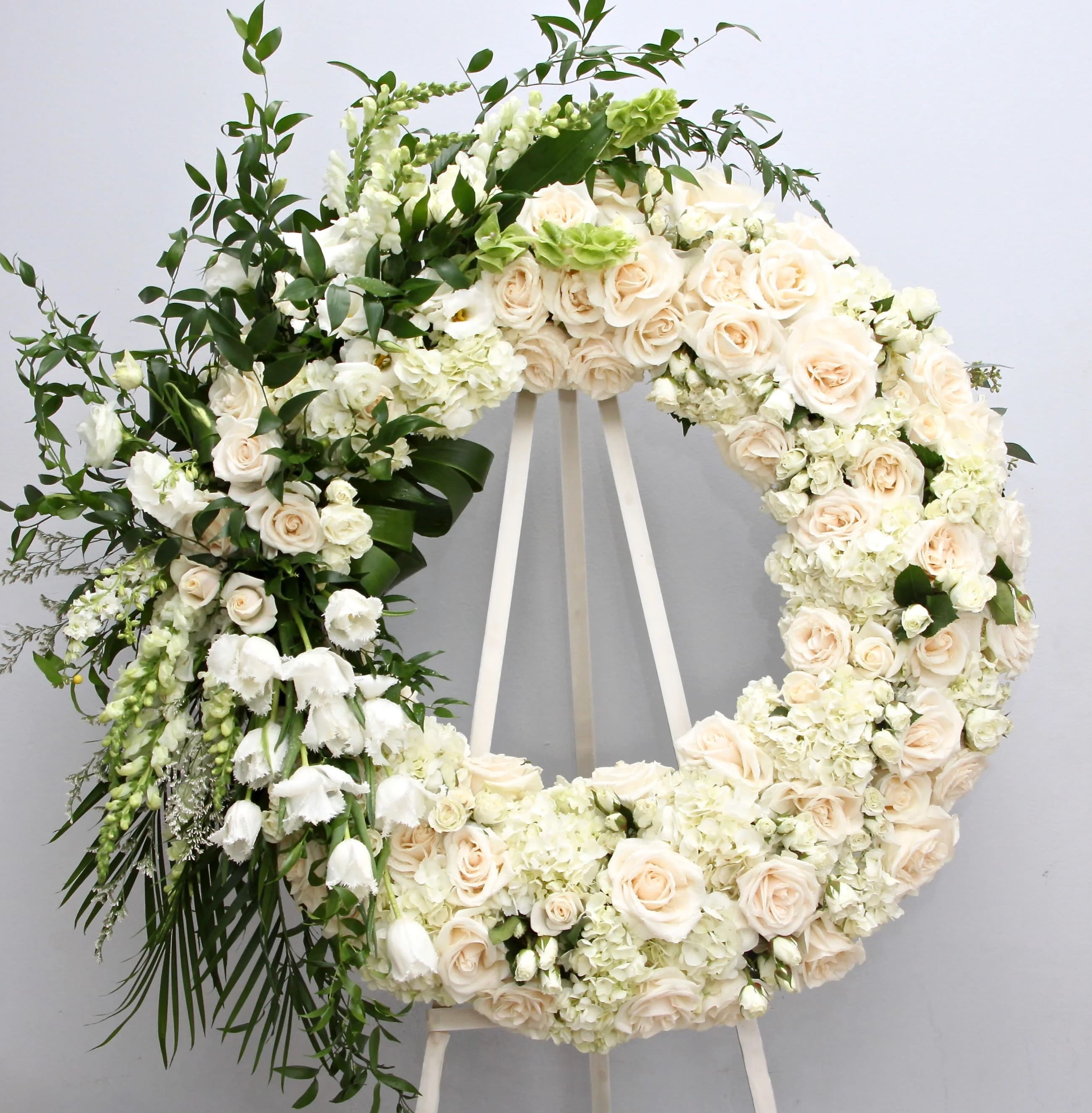 Large white floral wreath on an easel with cream roses and greenery