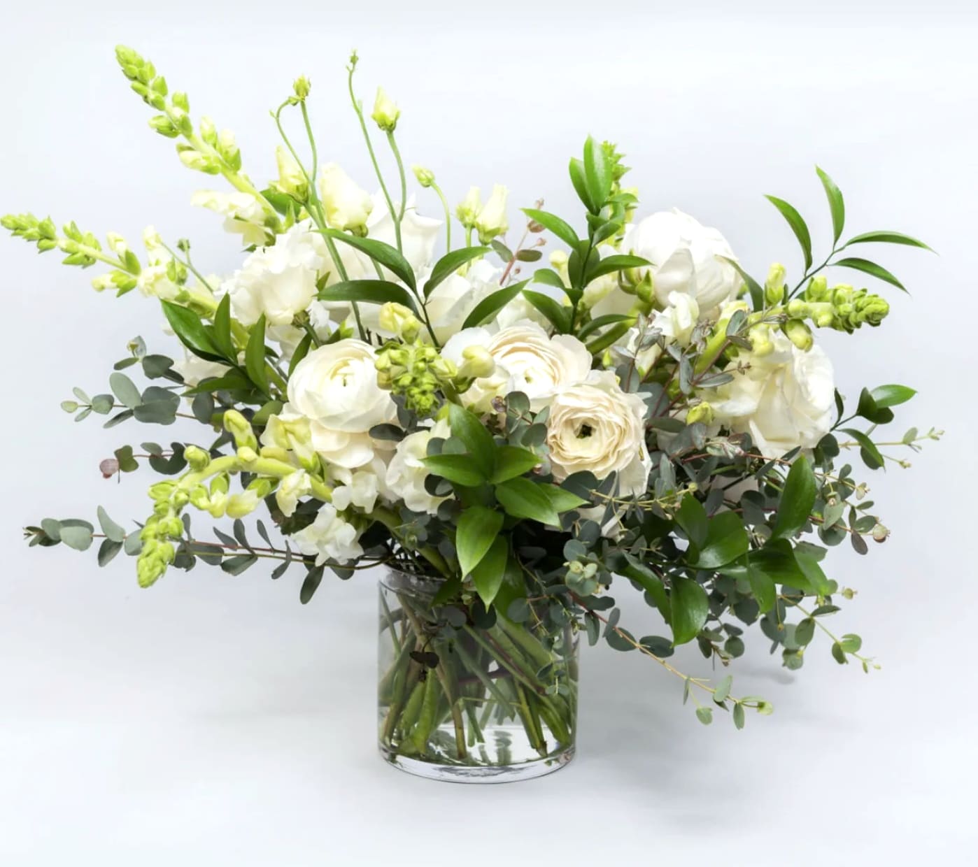 White floral arrangement in a clear glass vase with green foliage