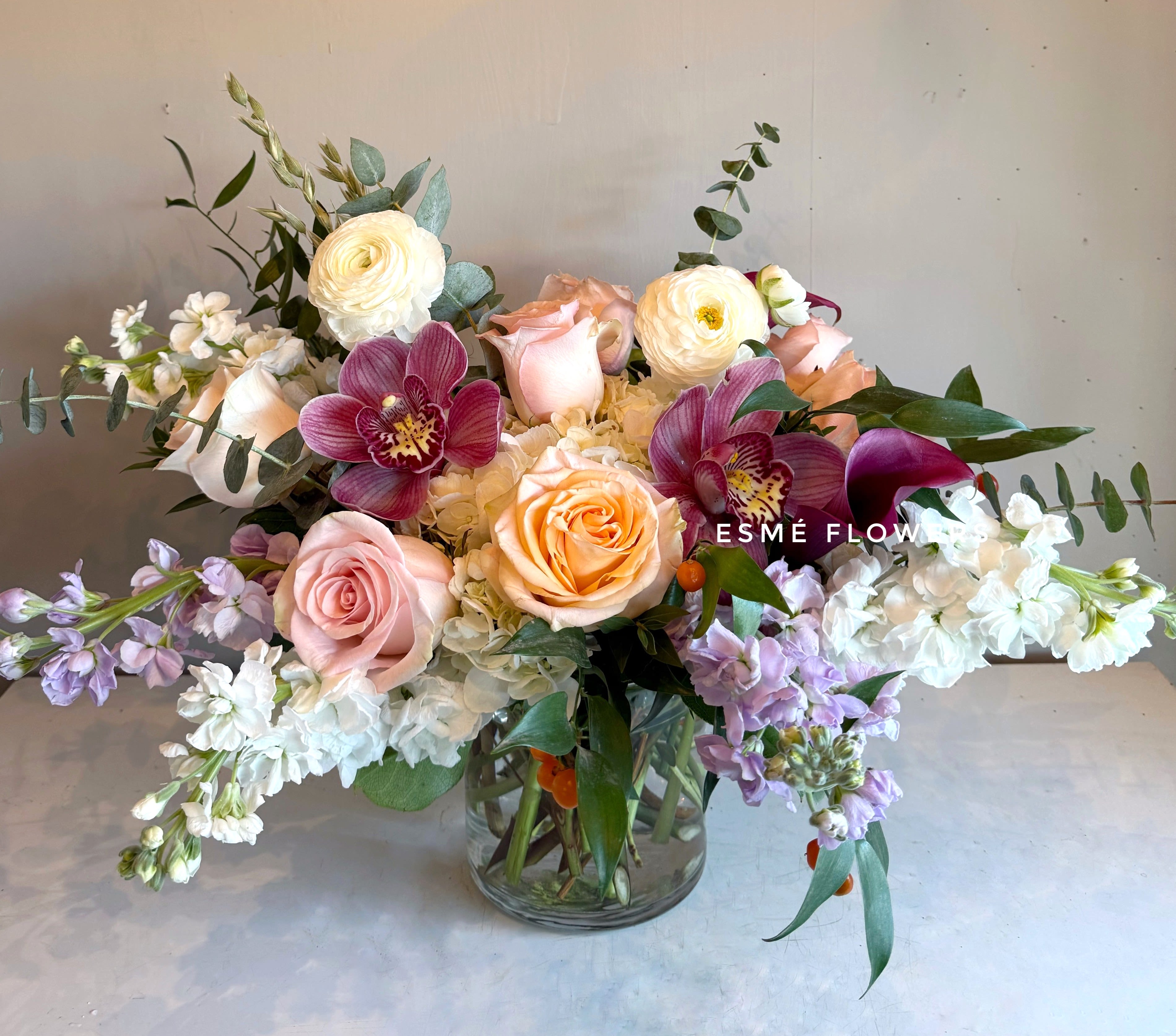 Mixed bouquet of roses, orchids, and white blooms in a glass vase