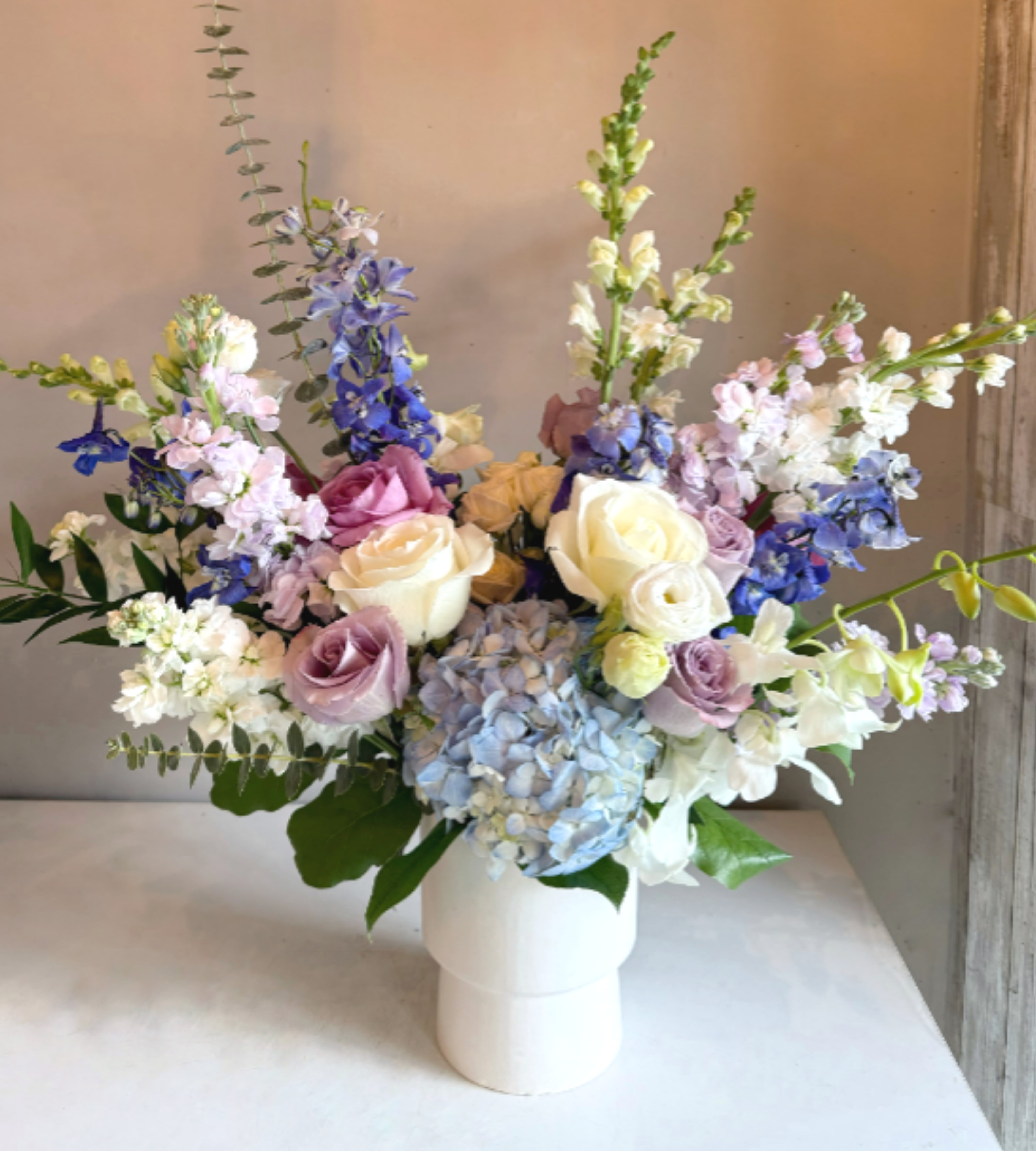 Celeste - This asymmetric arrangement exudes timeless elegance with a refined palette of blue, white, and lavender blooms. Carefully composed for a modern yet graceful look, it creates a sophisticated centerpiece perfect for any occasion. 