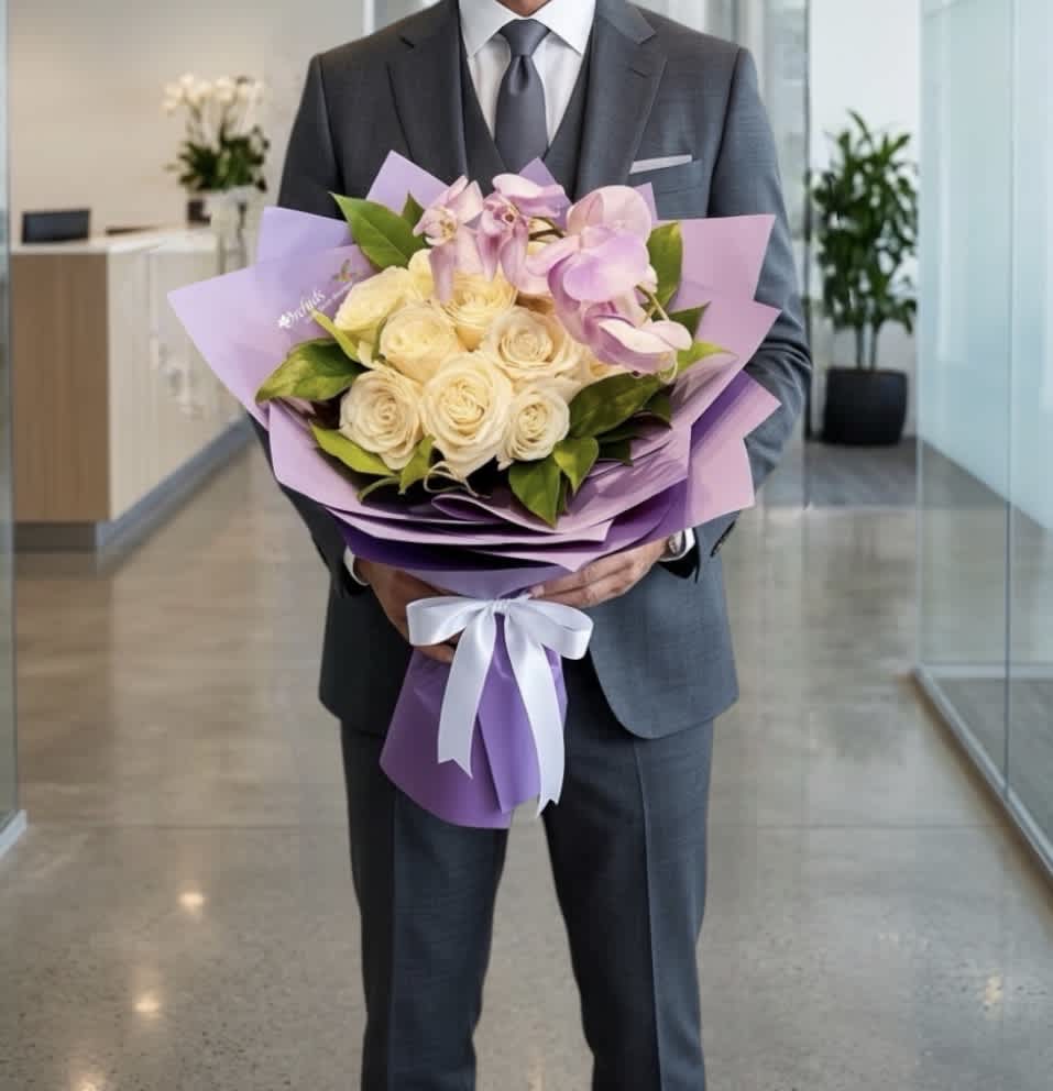 Man in a suit holding a bouquet of cream roses and pink orchids