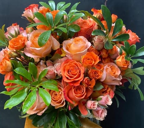 Bouquet of orange and peach roses with glossy green foliage