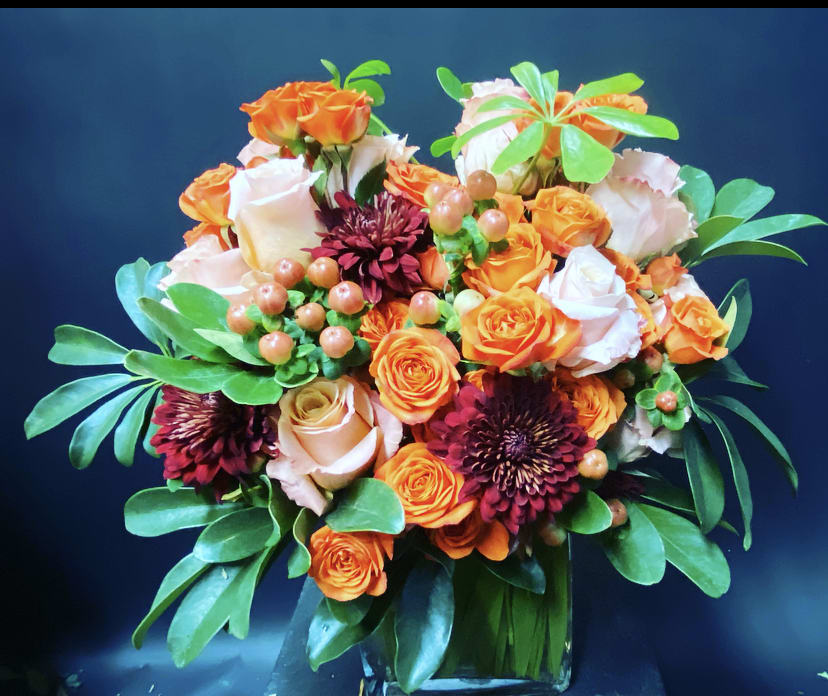 Bouquet of orange and white roses with dark burgundy blooms in a glass vase