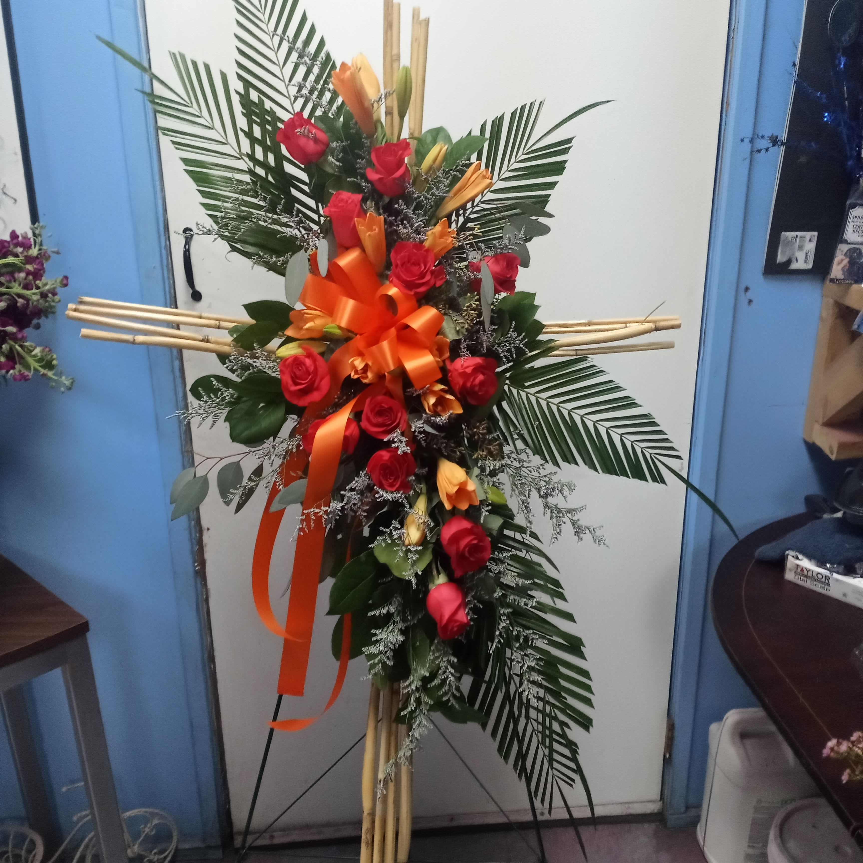 Tall standing floral spray with red roses and orange lilies on a bamboo easel