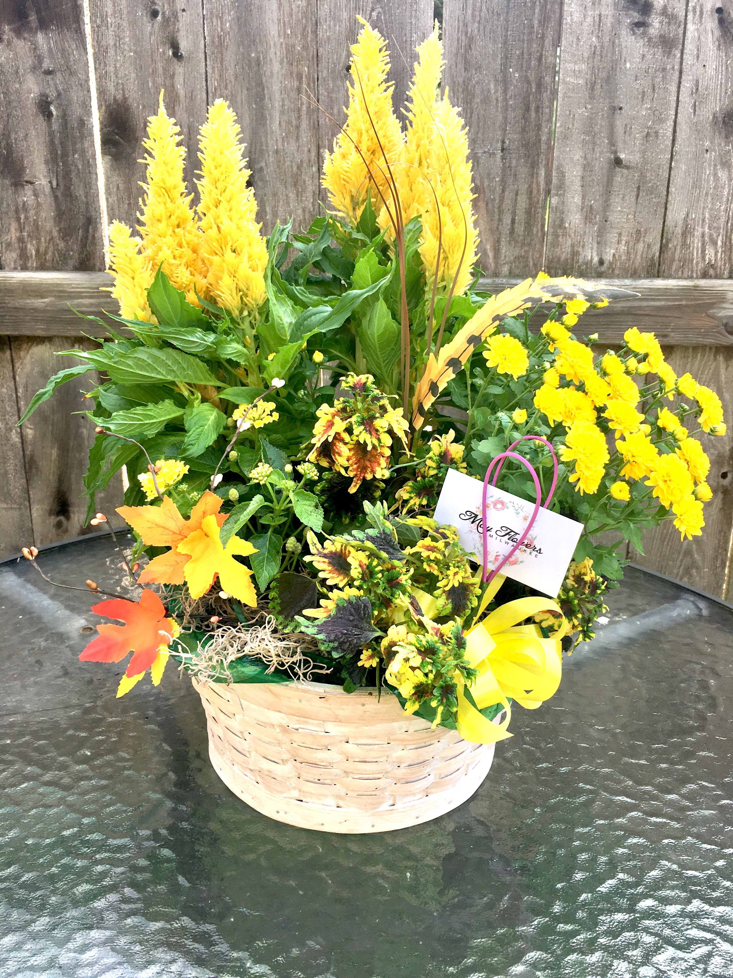 Basket of yellow flowering plants with tall plumes and a yellow bow on a glass table