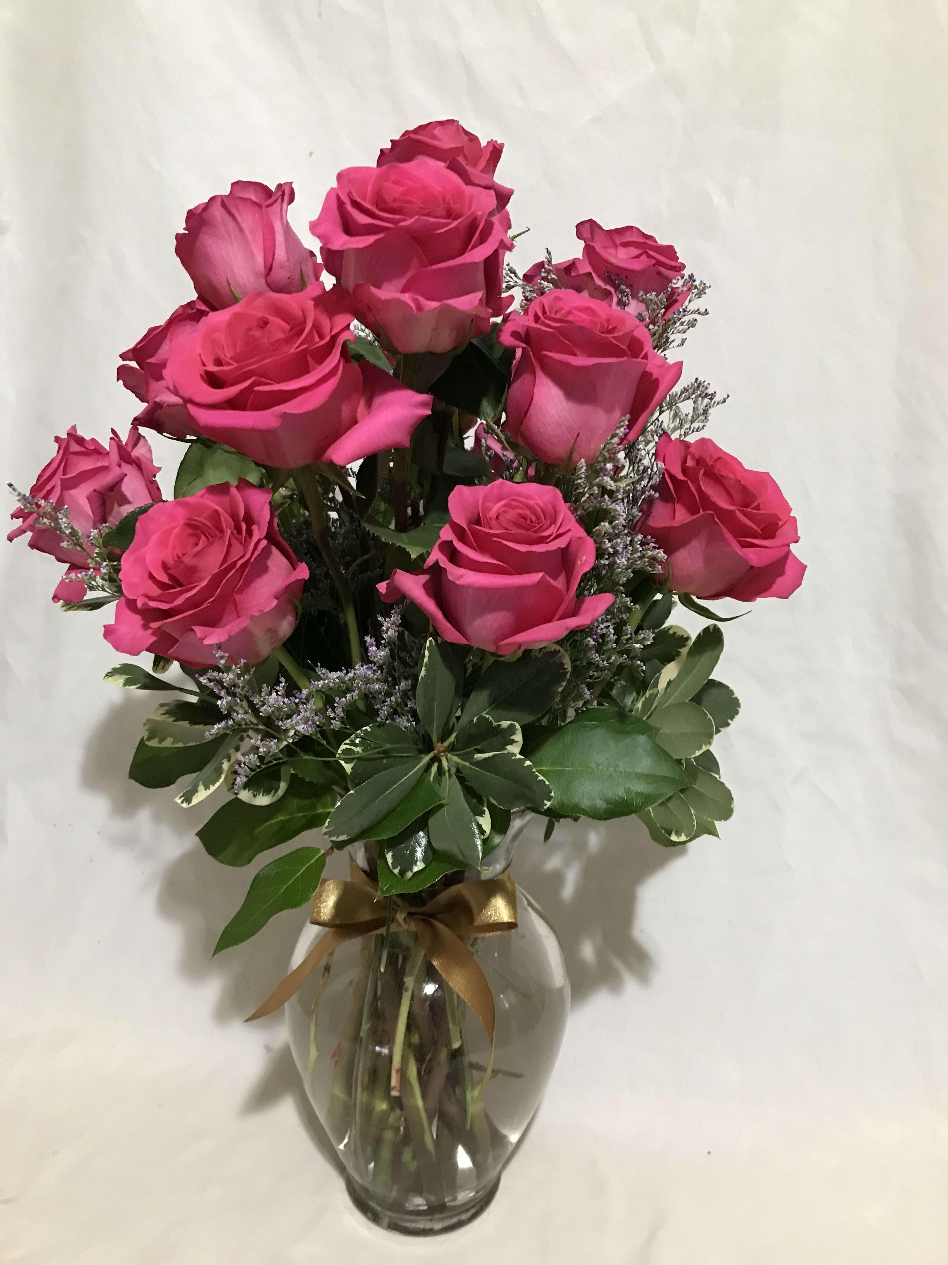 Arrangement of bright pink roses with filler blooms in a clear glass vase tied with a gold ribbon.