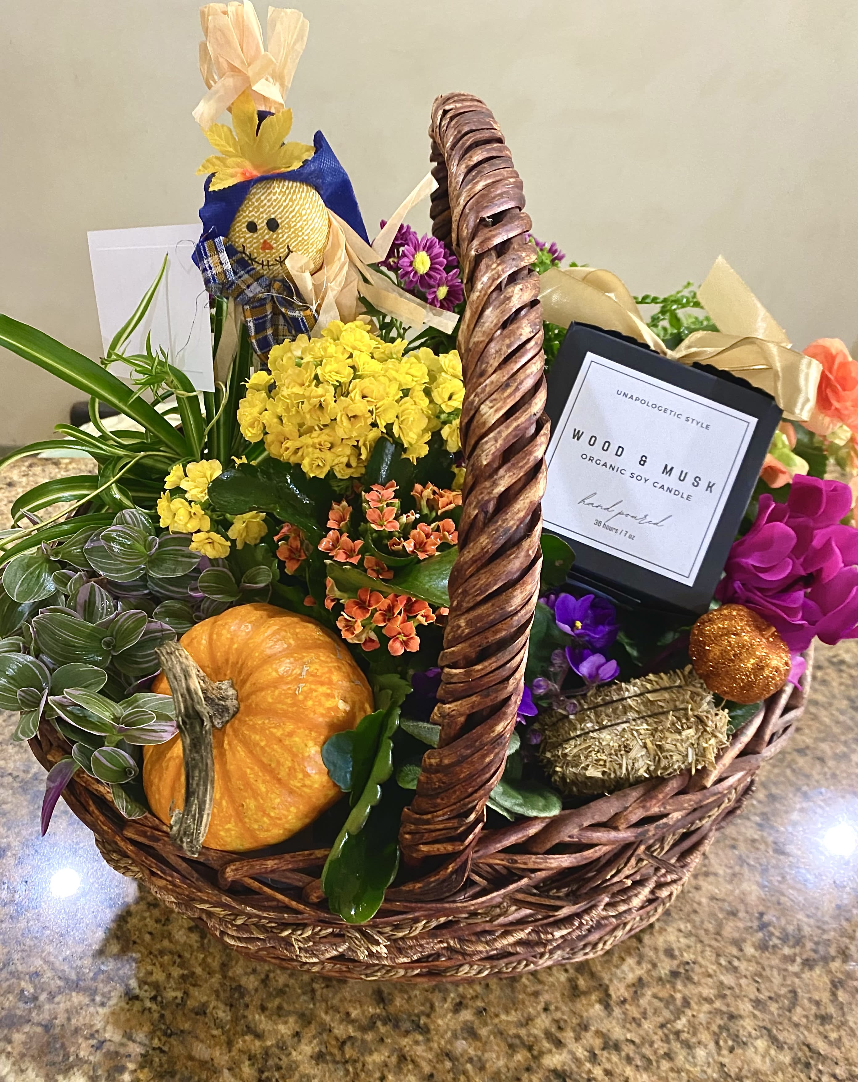 Autumn gift basket with yellow and orange flowering plants, a pumpkin, candle, and fall decorations