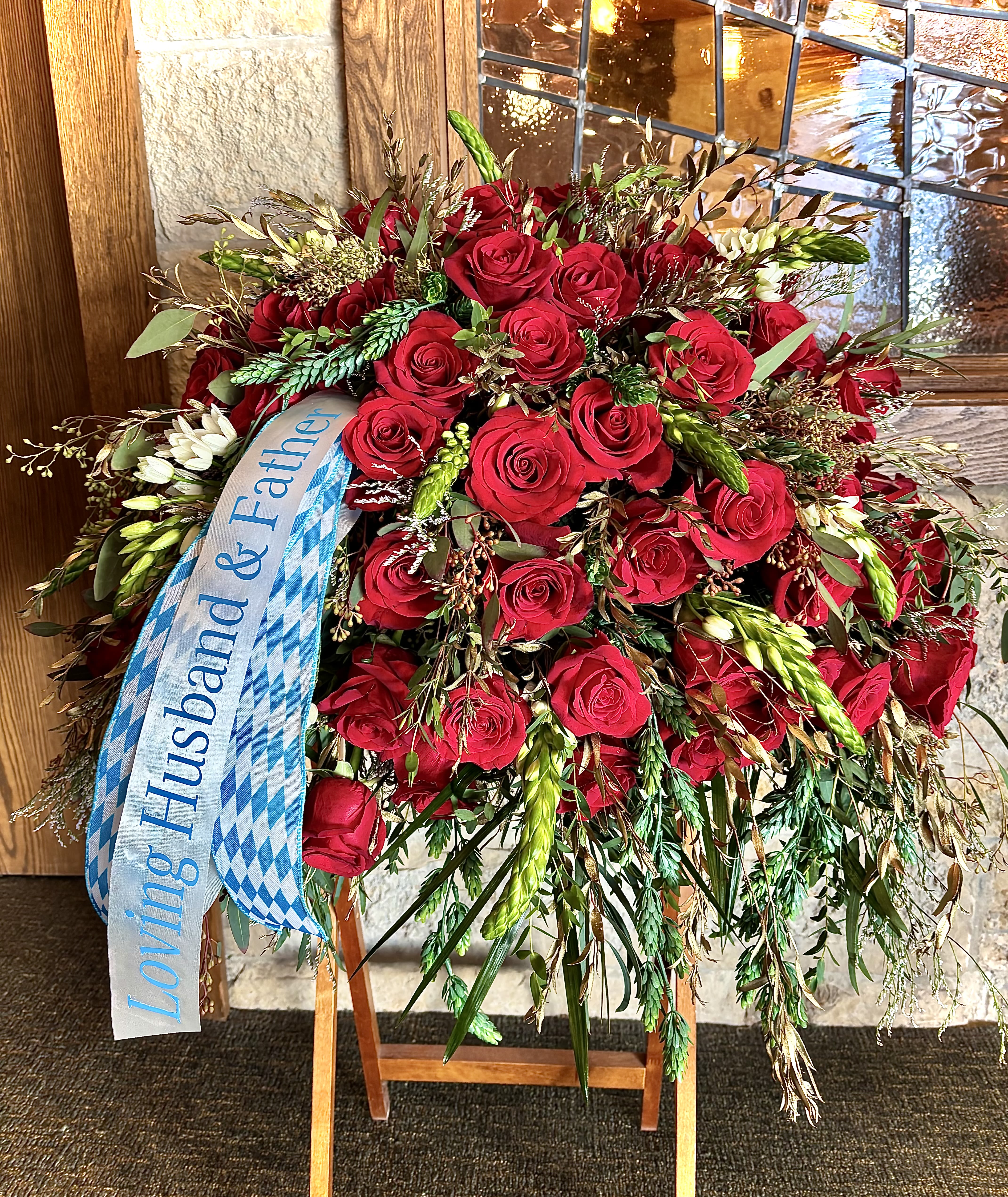 Tall standing spray of red roses with cascading greenery and a memorial ribbon on an easel.