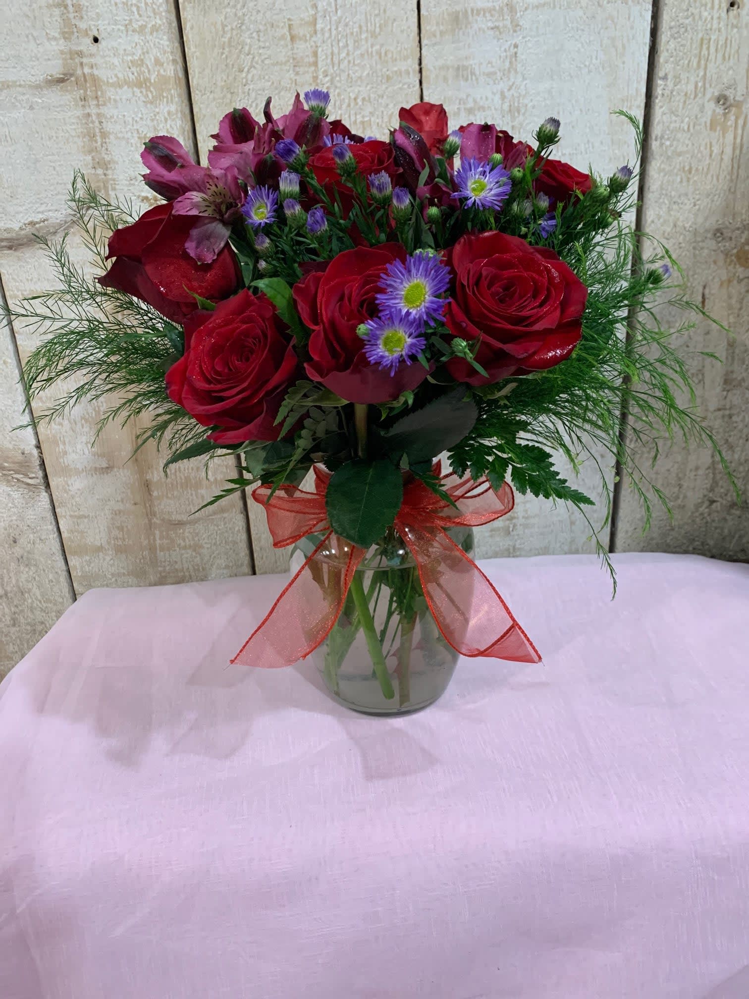 Bouquet of red roses and purple flowers in a glass vase with a red ribbon
