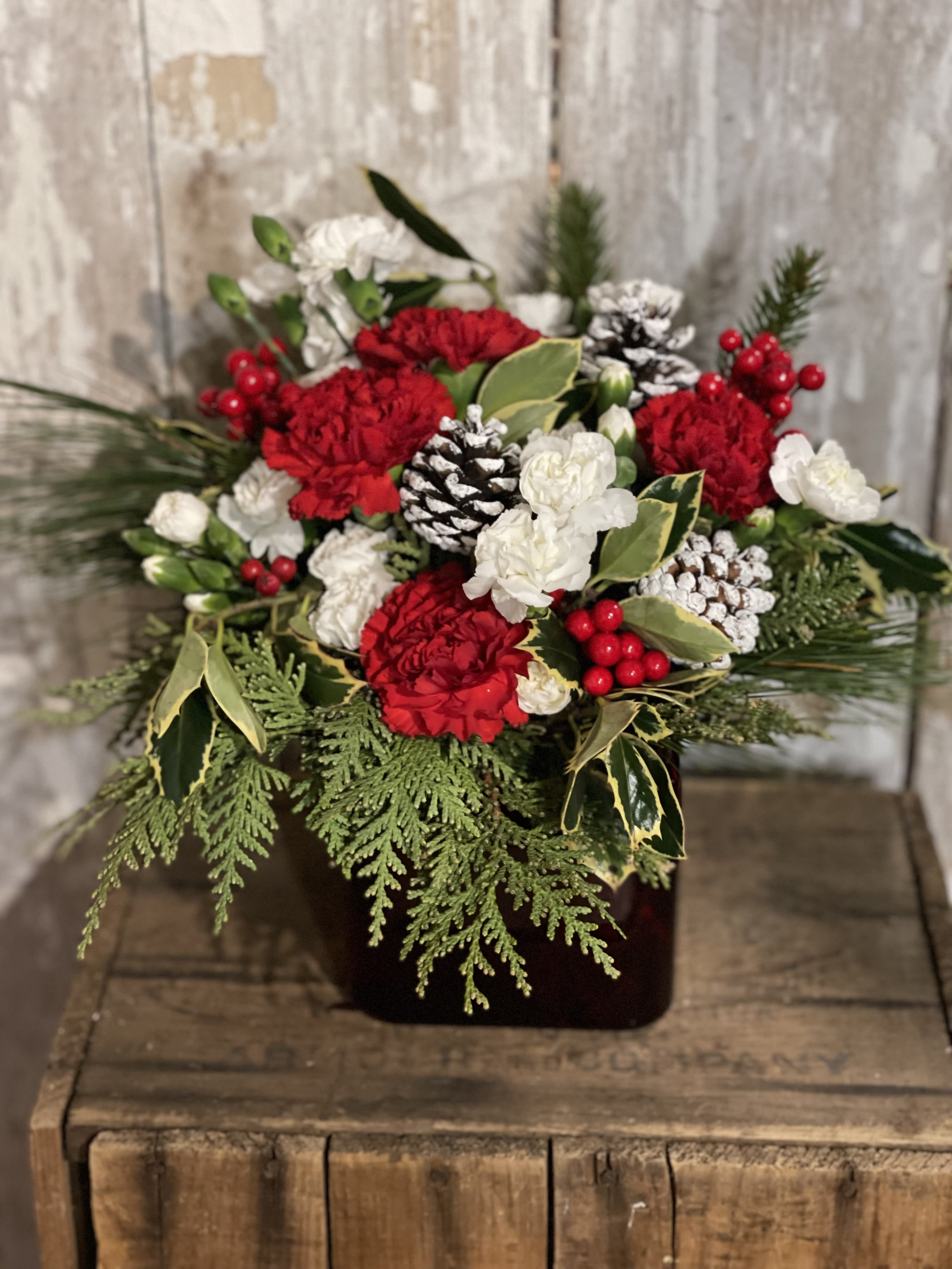 Red and white floral arrangement with pinecones in a dark container