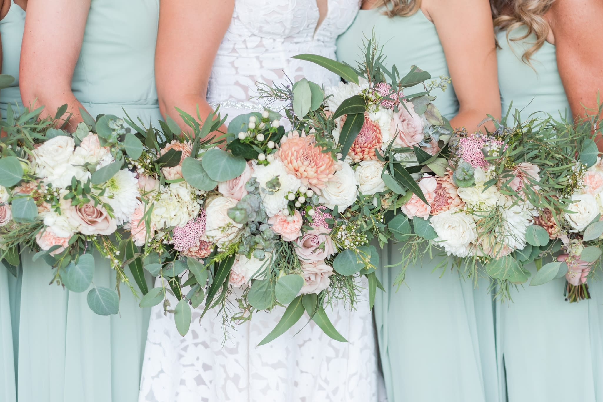 Bridesmaids holding pastel bouquets with roses and greenery