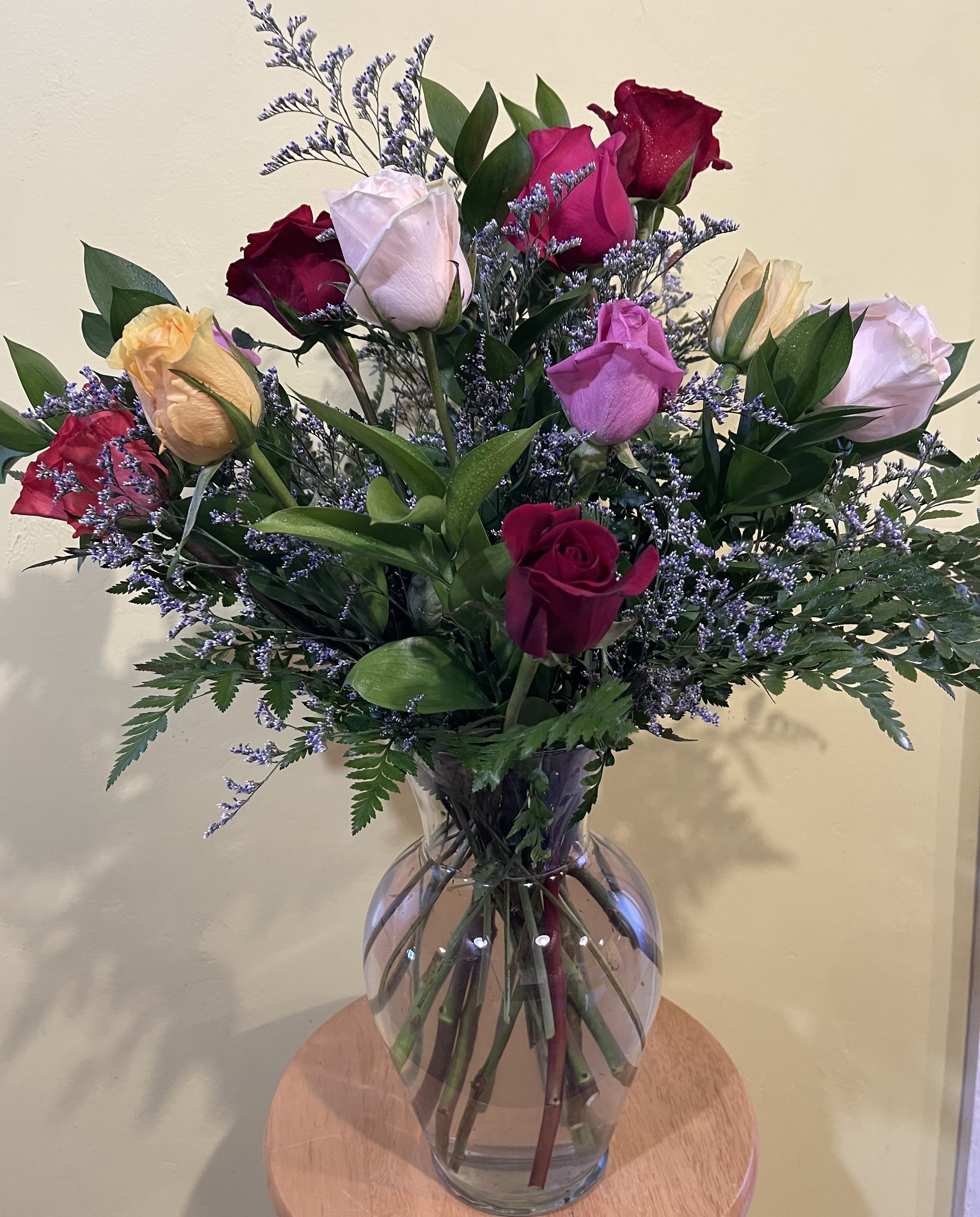 Mixed roses in a clear glass vase with purple filler flowers