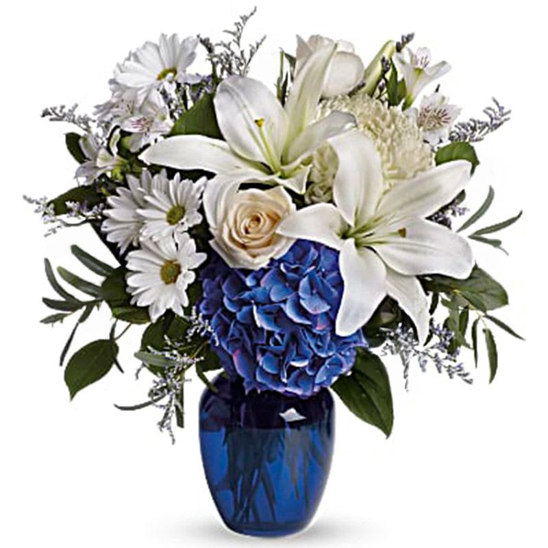 White lilies and daisies arranged in a blue vase with a blue hydrangea